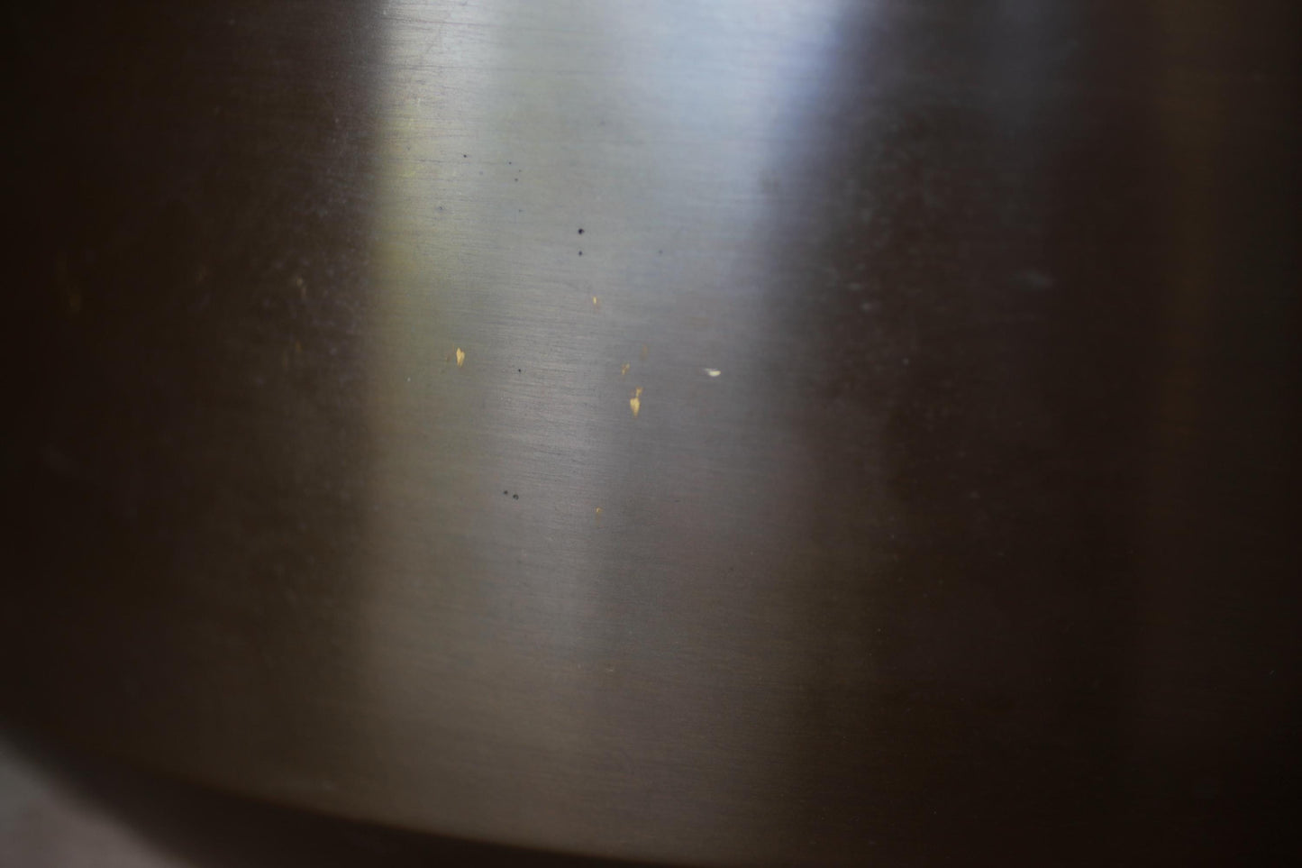 a close-up view of a metal surface with a few small scratches and stains, giving it a slightly worn and aged appearance.