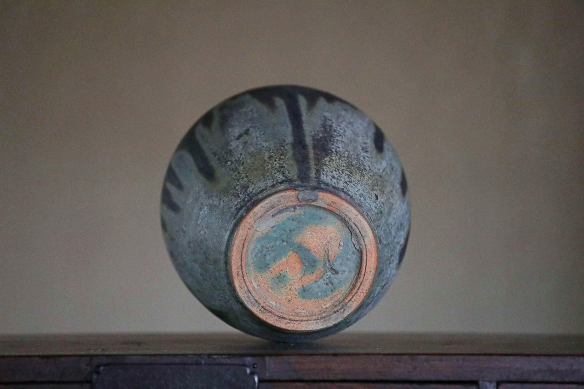 A ceramic vase with a blue and orange patterned design sits on a wooden surface against a plain background.