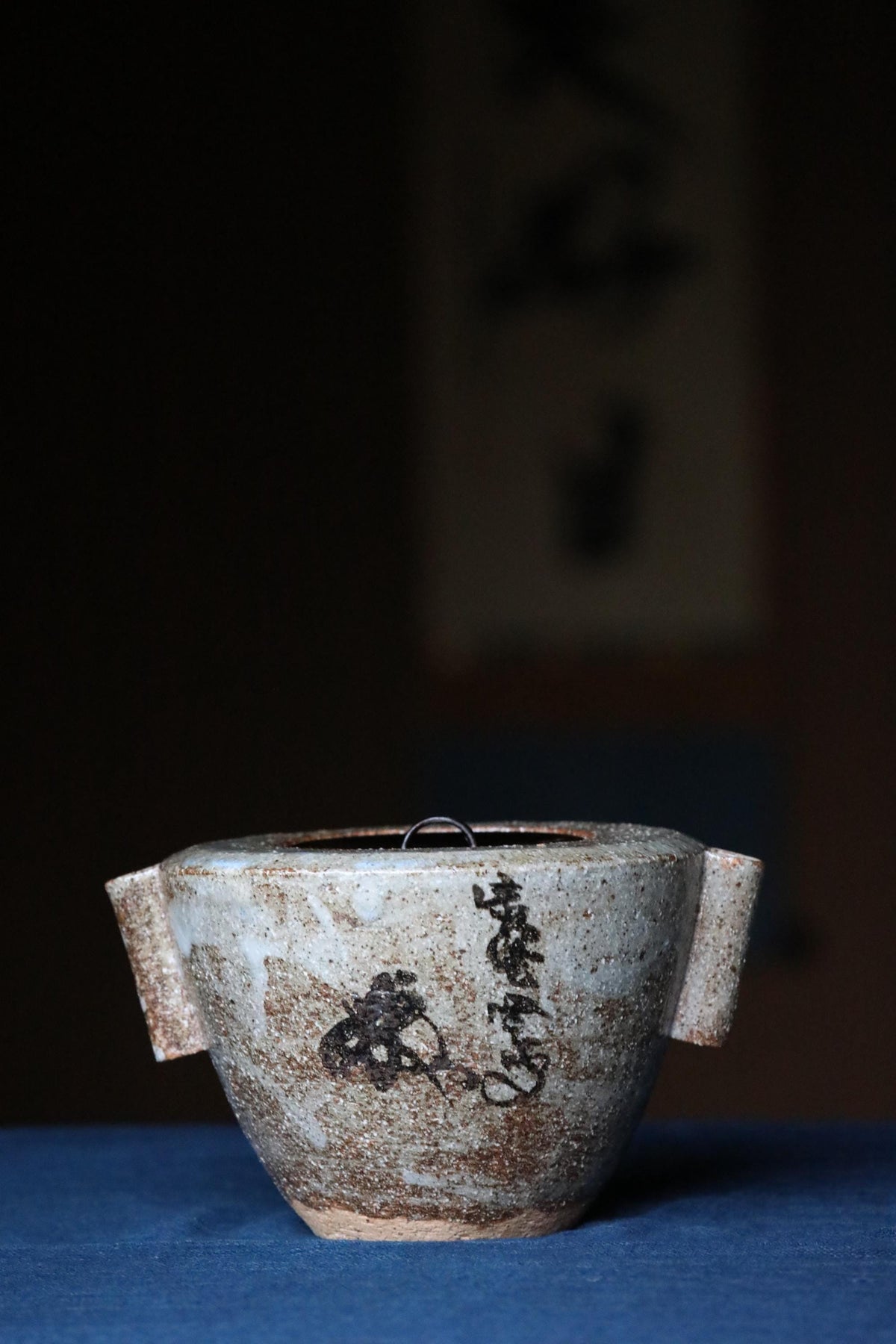 A ceramic teapot with a black design on its surface, sitting on a blue surface.