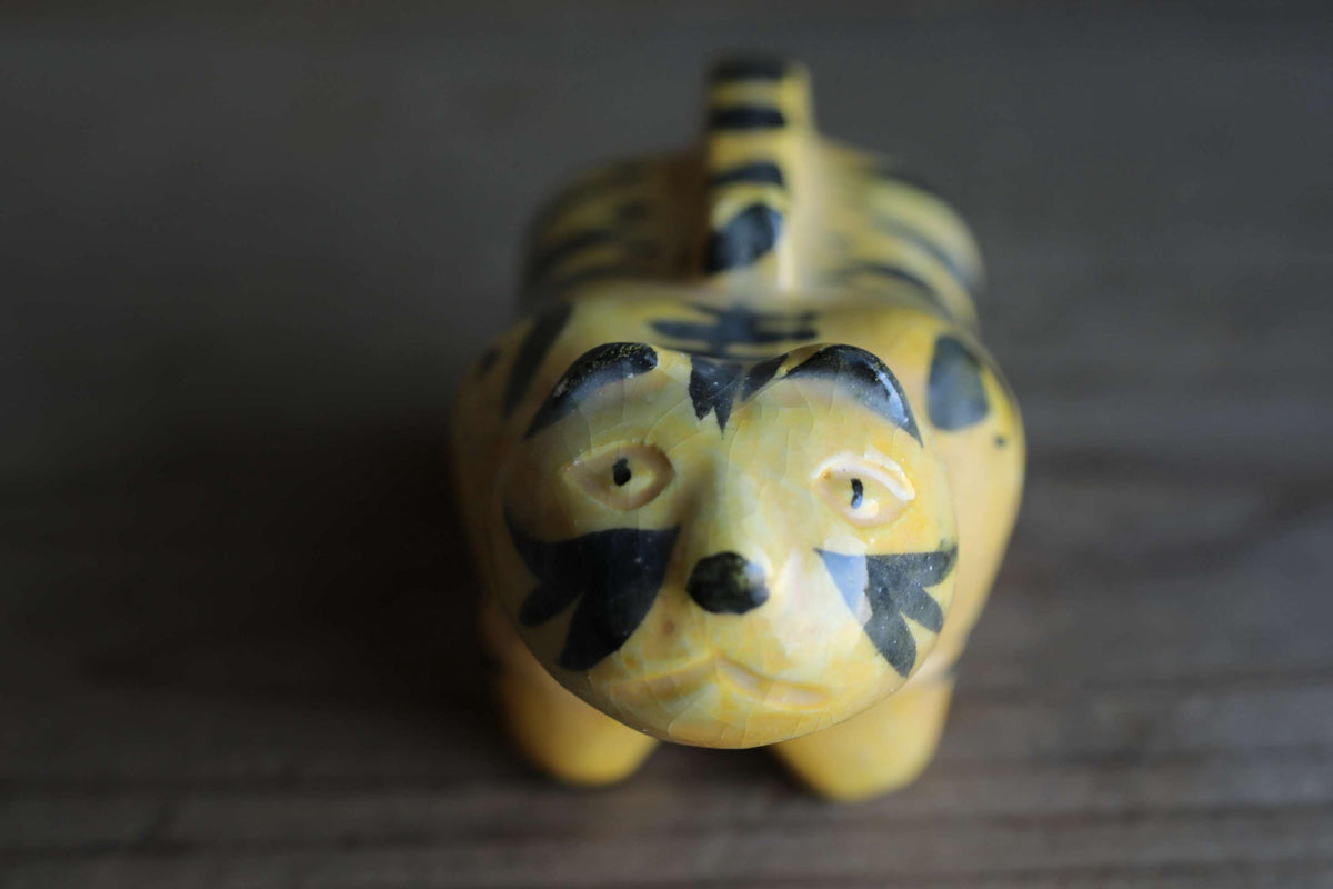 A yellow and black tiger figurine with a pointed nose and large eyes, sitting on a wooden surface.