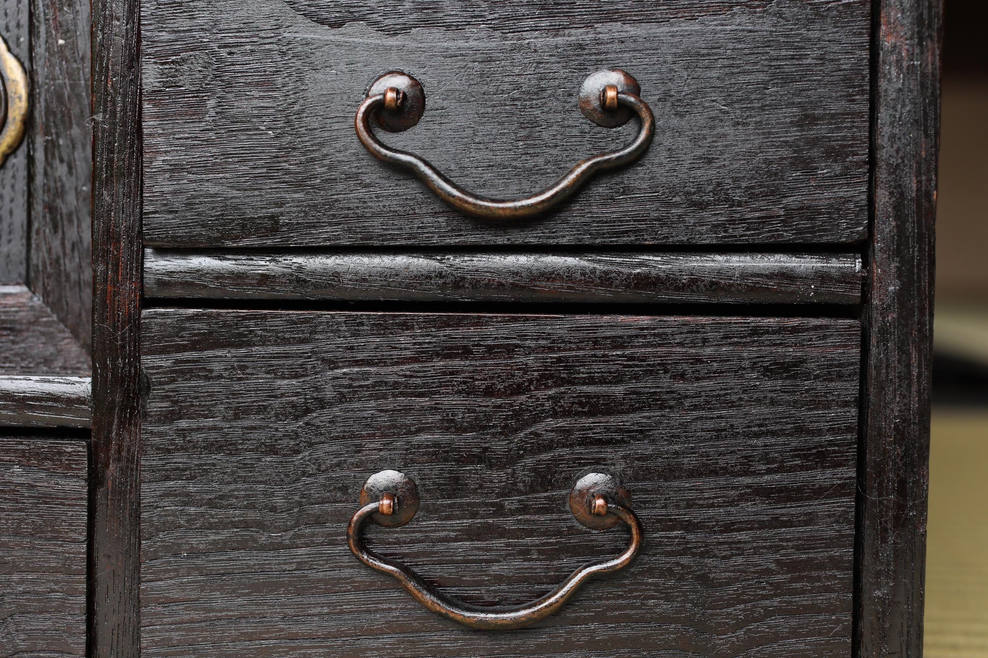 a close-up view of a dark wooden drawer with two metal handles, likely made of brass or a similar material.