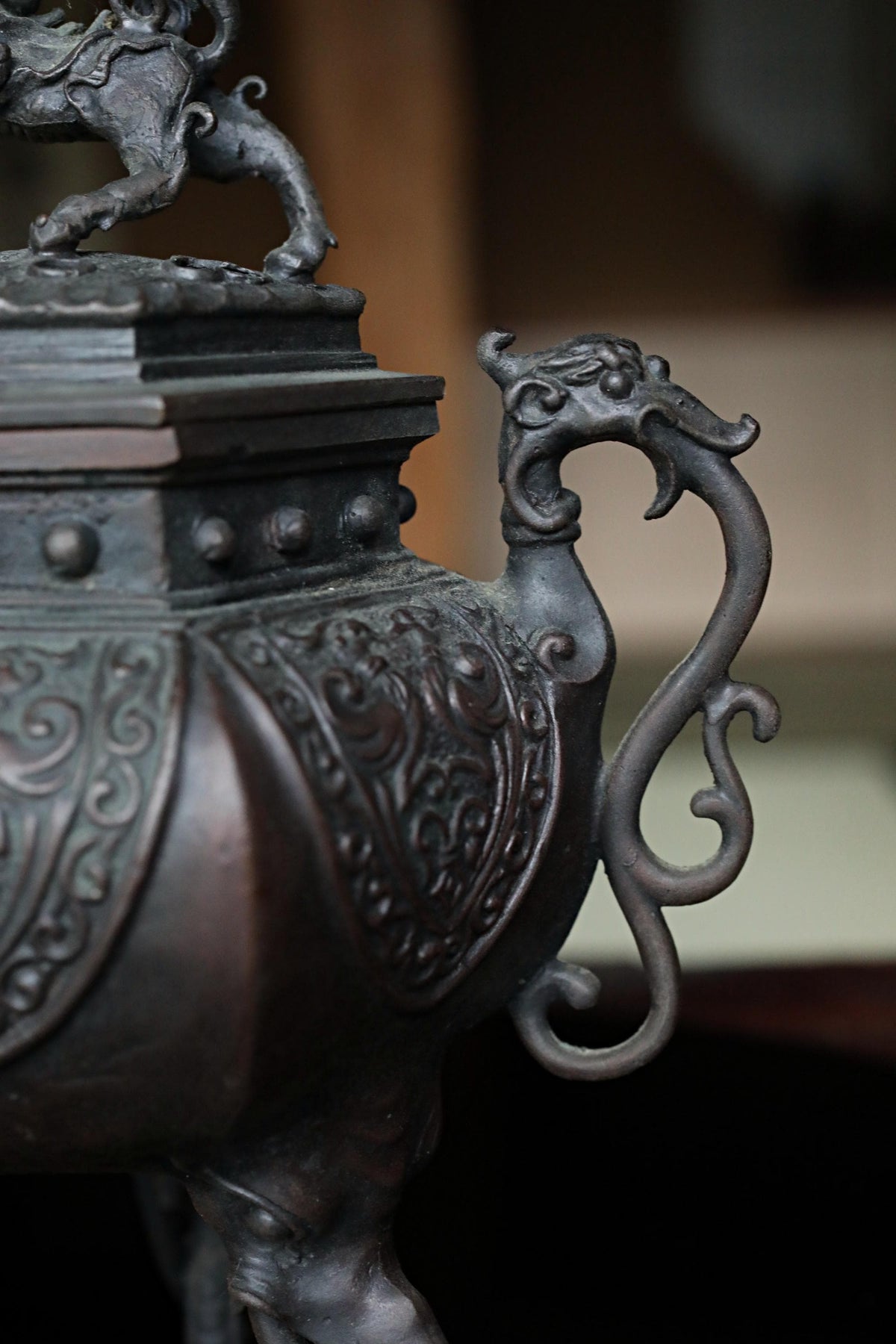 A close-up view of an ornate, dark-colored metal object, possibly a vase or urn, with intricate designs and patterns.