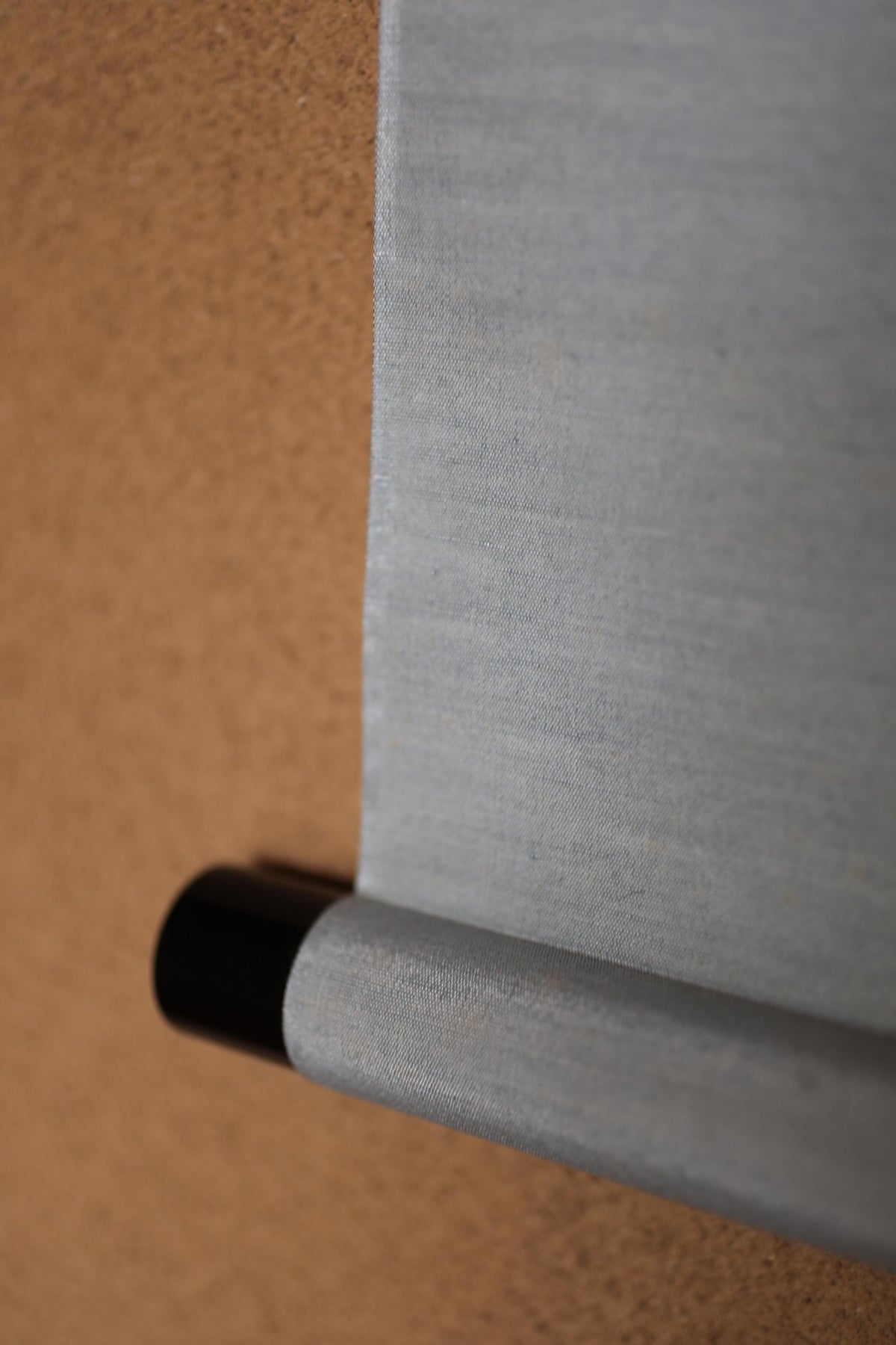 a close-up view of a grey fabric or material, possibly a piece of clothing or a textile, with a black object or end piece attached to it.