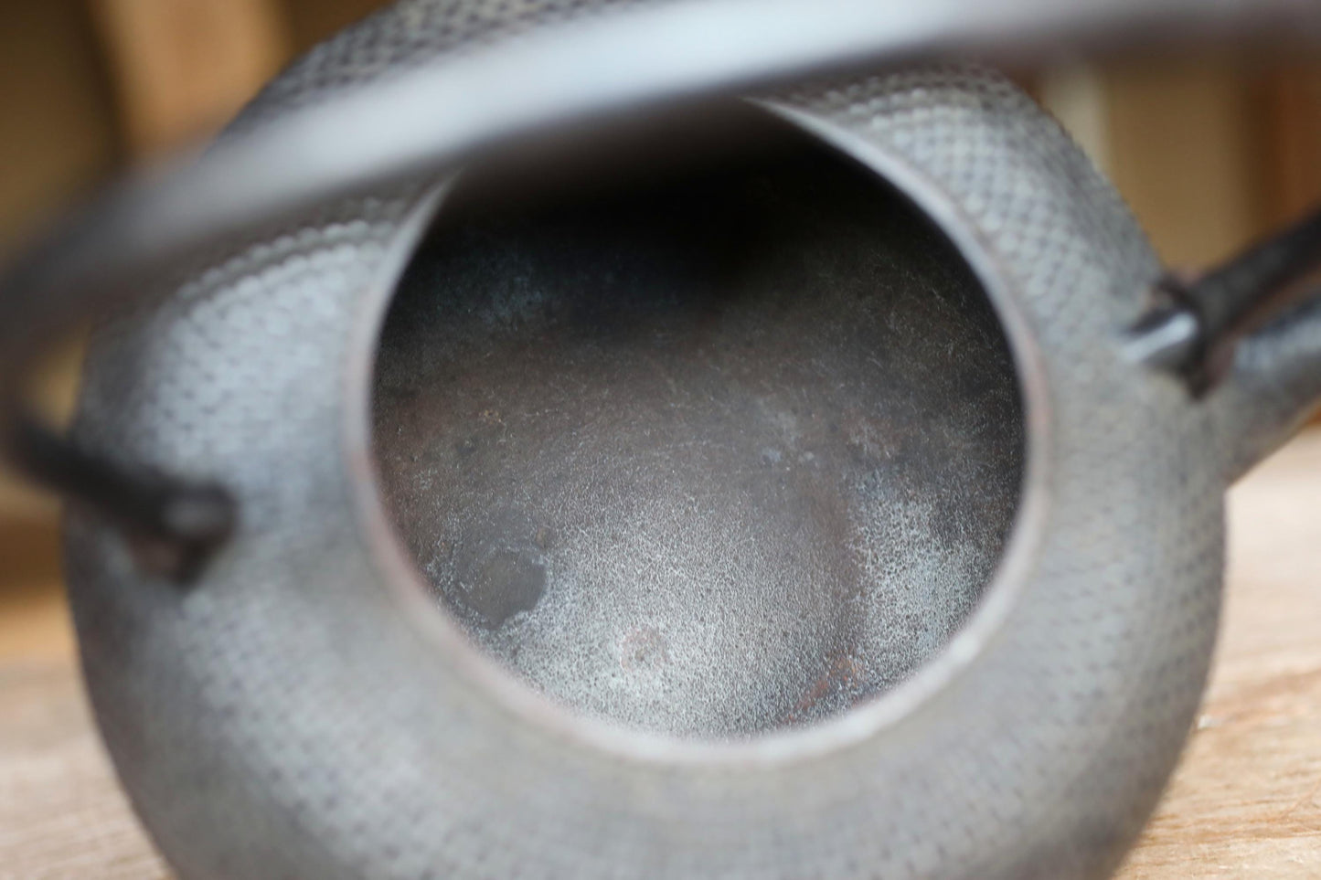 A close-up view of a black metal teapot with a textured surface, featuring a small hole in the center.