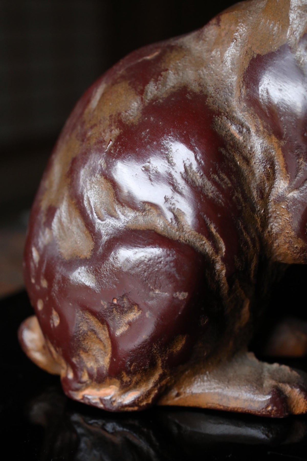 A close-up view of a dark brown, textured metal sculpture with a shiny, maroon-colored surface.