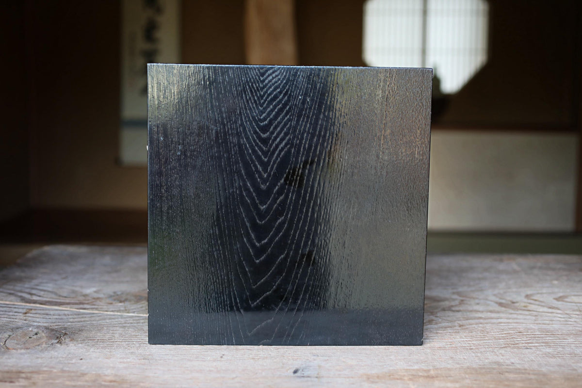 a square, dark-colored surface with a textured, wood-like appearance, placed on a wooden surface.