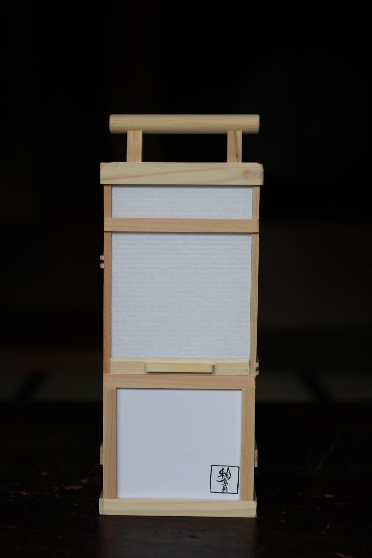 A wooden frame with a blank white sheet of paper inside, placed on a dark surface.