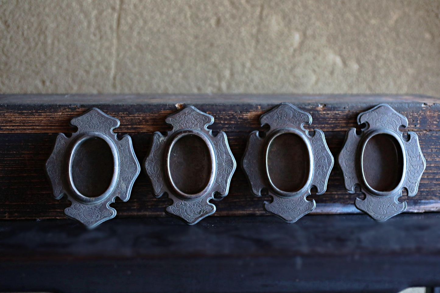 a row of four ornate metal handles or knobs, each with a unique design, attached to a dark wooden surface.
