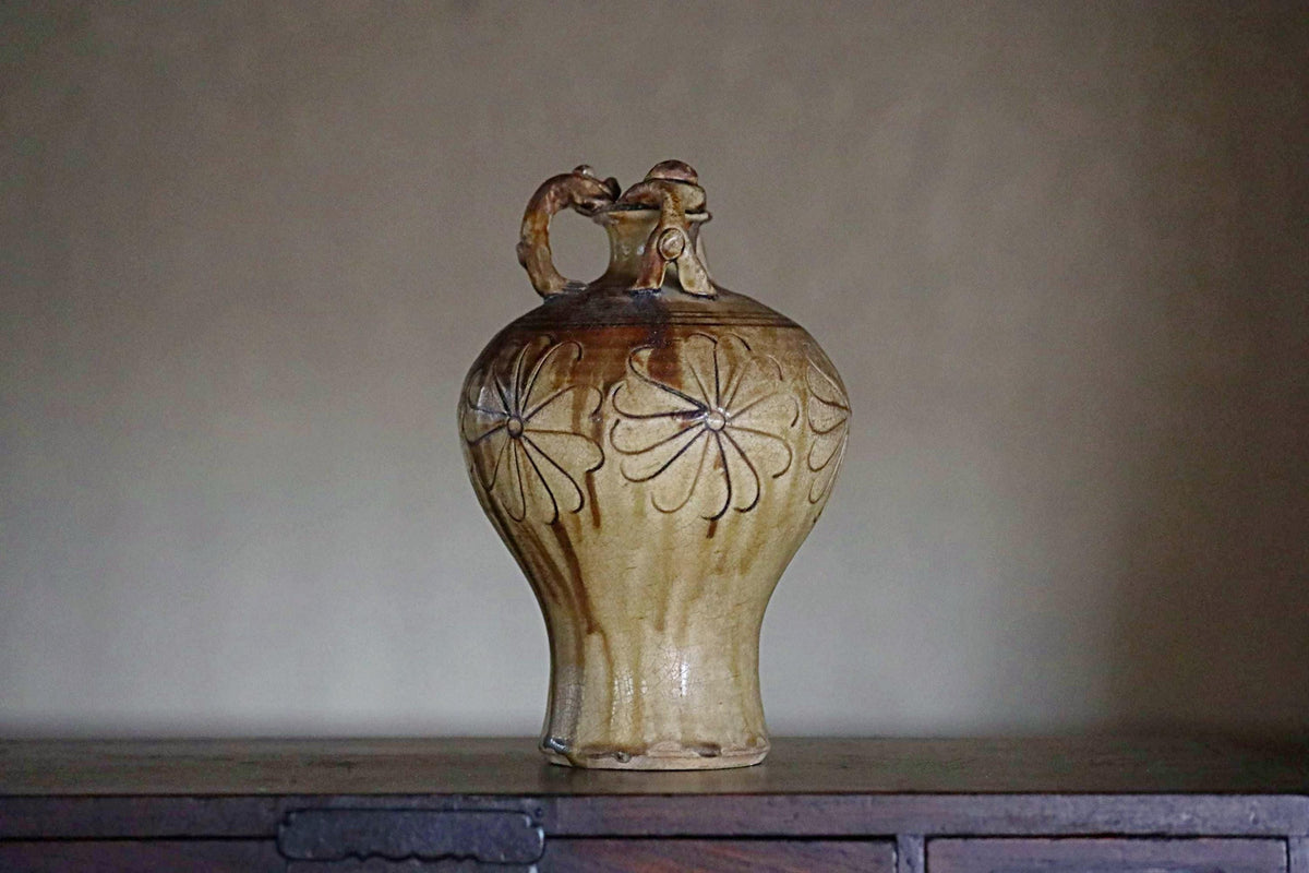 A ceramic vase with a floral design sits on a wooden surface against a plain background.