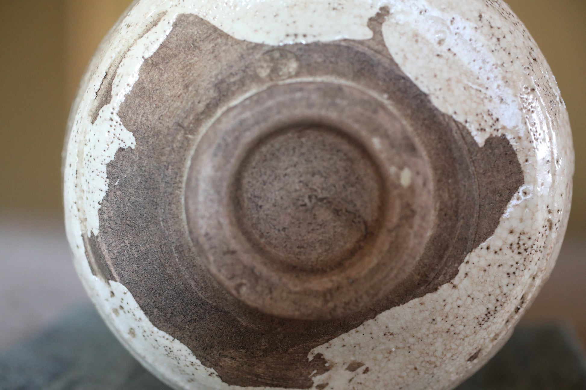 A close-up view of a ceramic bowl or vase with a speckled, speckled, and speckled pattern, featuring a central hole or opening.