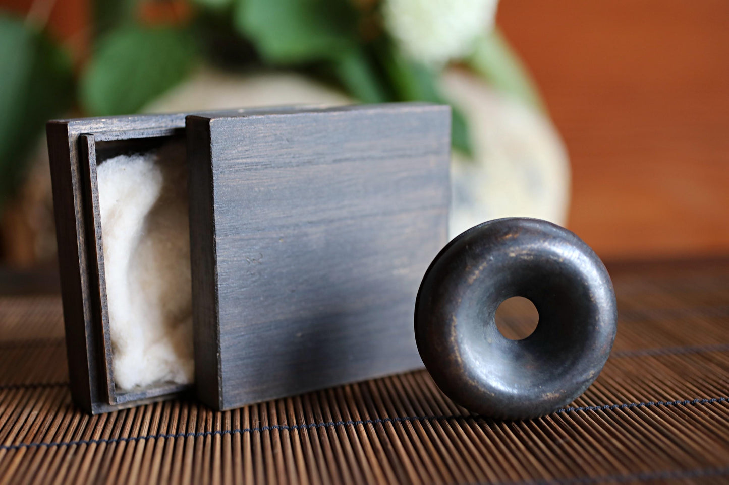 a wooden box with a white cloth inside, and a black metal object with a hole in it placed next to the box on a wooden surface.