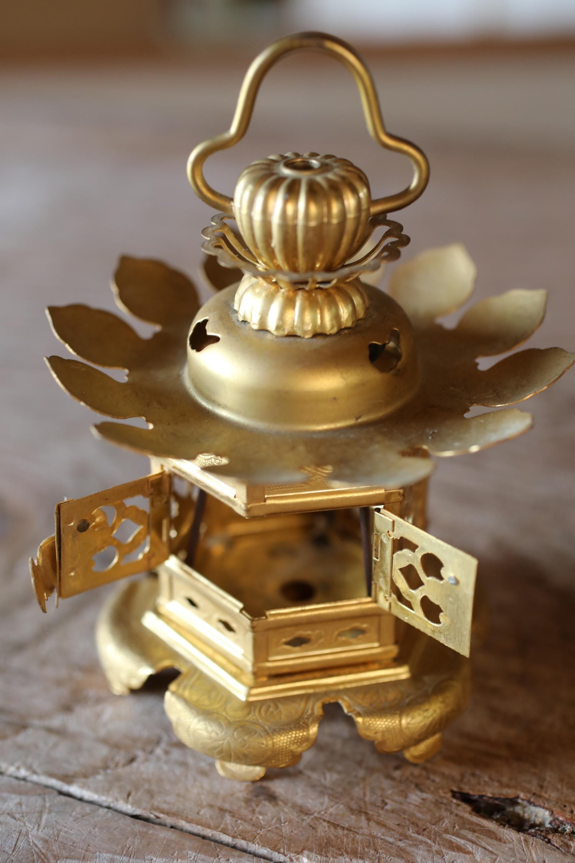 A golden, ornate lantern with a handle and a decorative lid sits on a wooden surface.