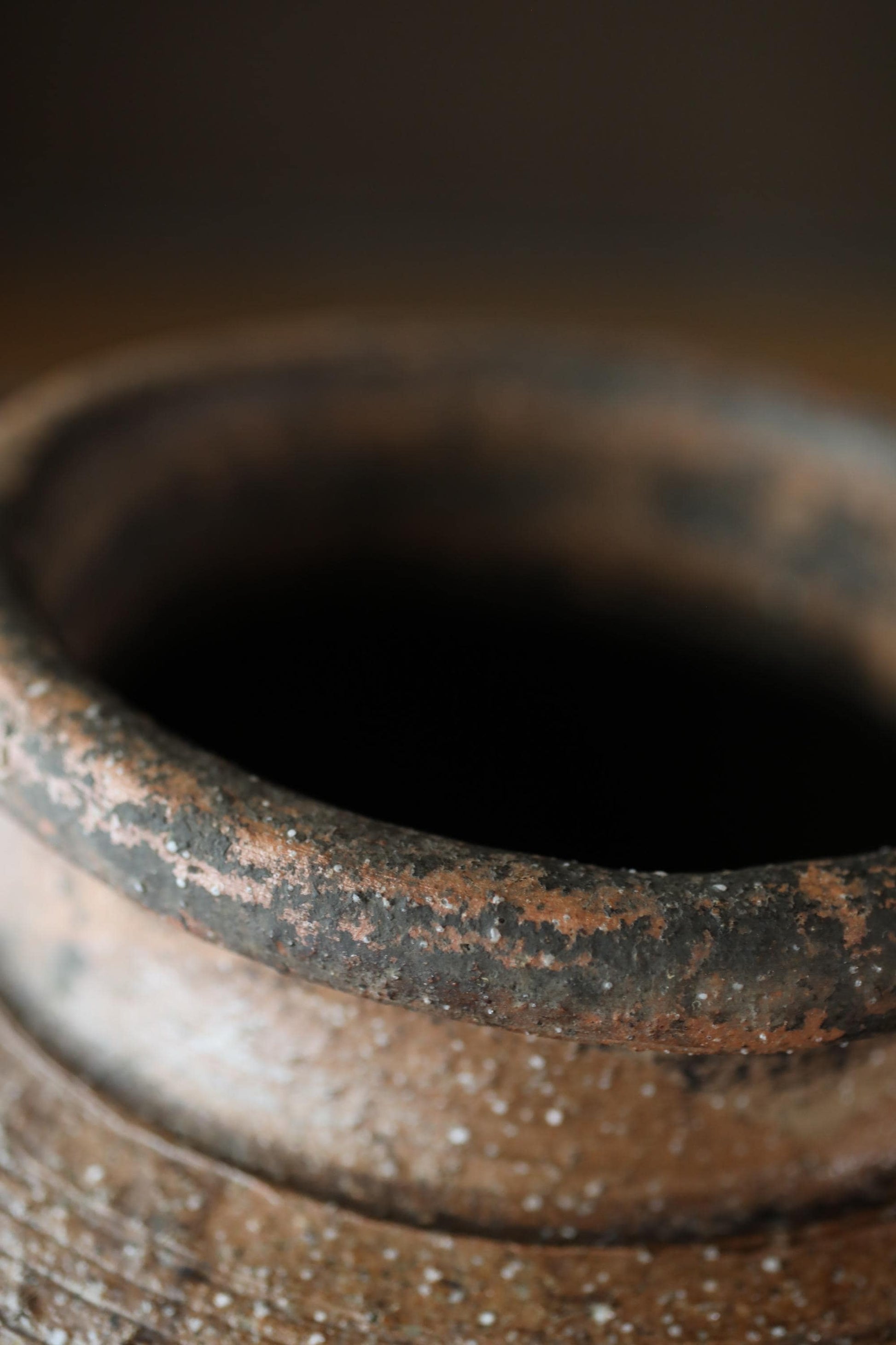 A close-up view of a rusted, weathered vase or container with a dark interior.