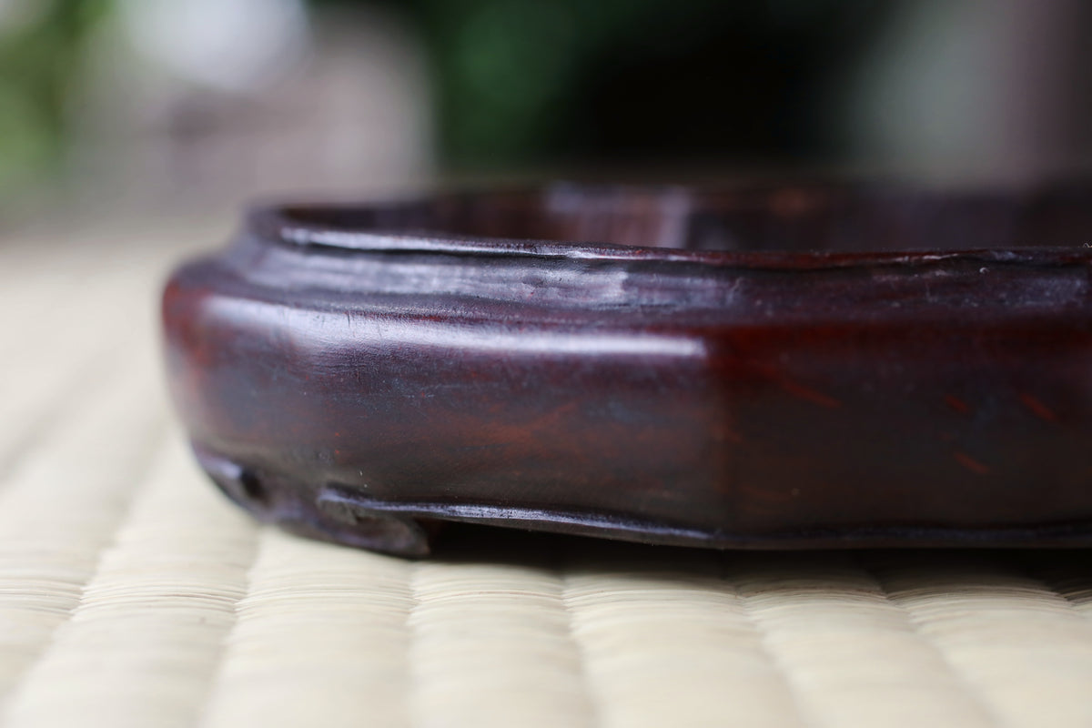 A close-up image of a dark wooden object, possibly a piece of furniture or a decorative item, resting on a woven surface.