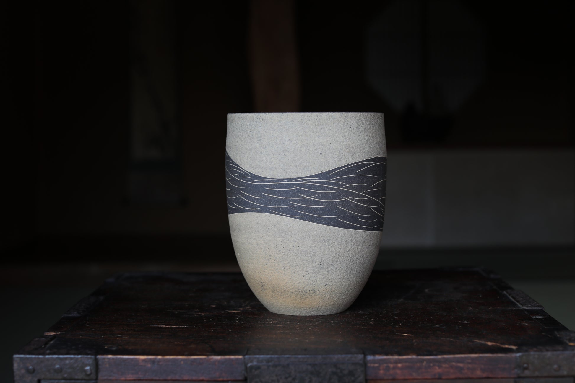 A ceramic vase with a black and white design on its surface, placed on a wooden surface.