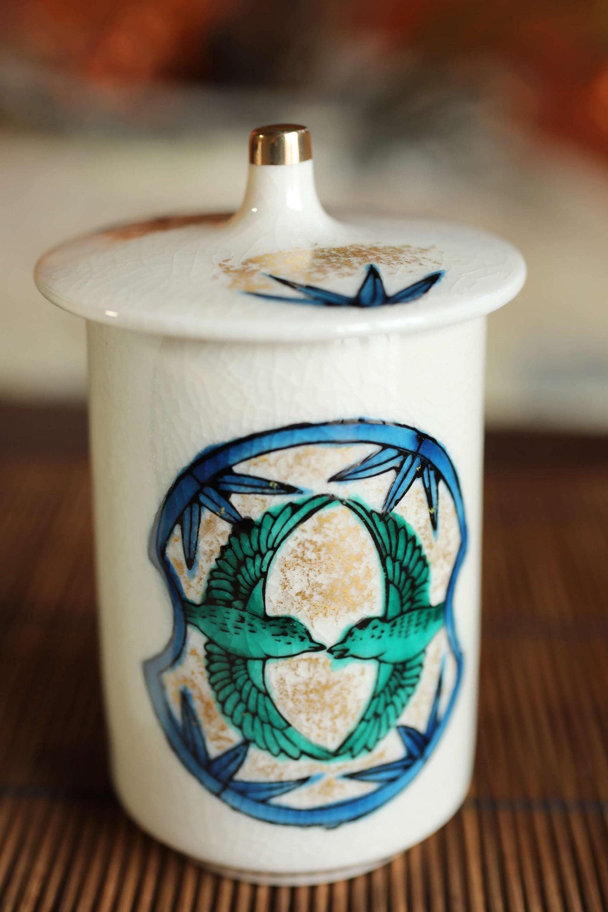 A white ceramic jar with a decorative blue and green design featuring two stylized birds.