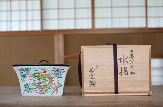 a ceramic container with a dragon design and a wooden box with Japanese text on it, both placed on a wooden surface.