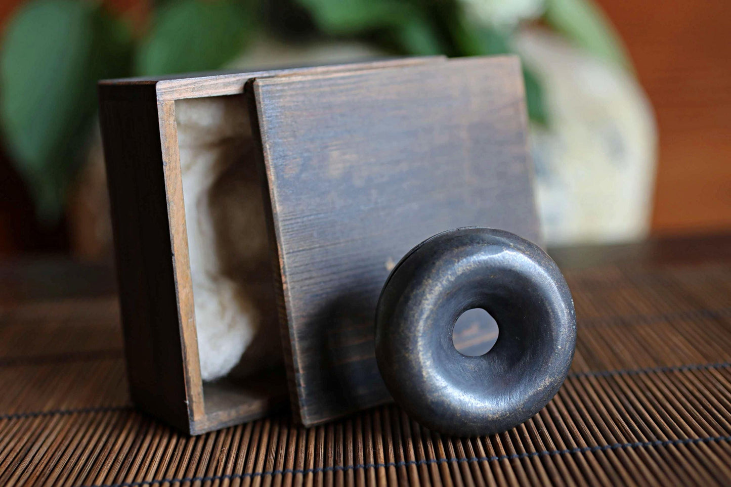 a wooden box with a lid, and a round metal object, possibly a sculpture or a piece of jewelry, placed on a bamboo mat.