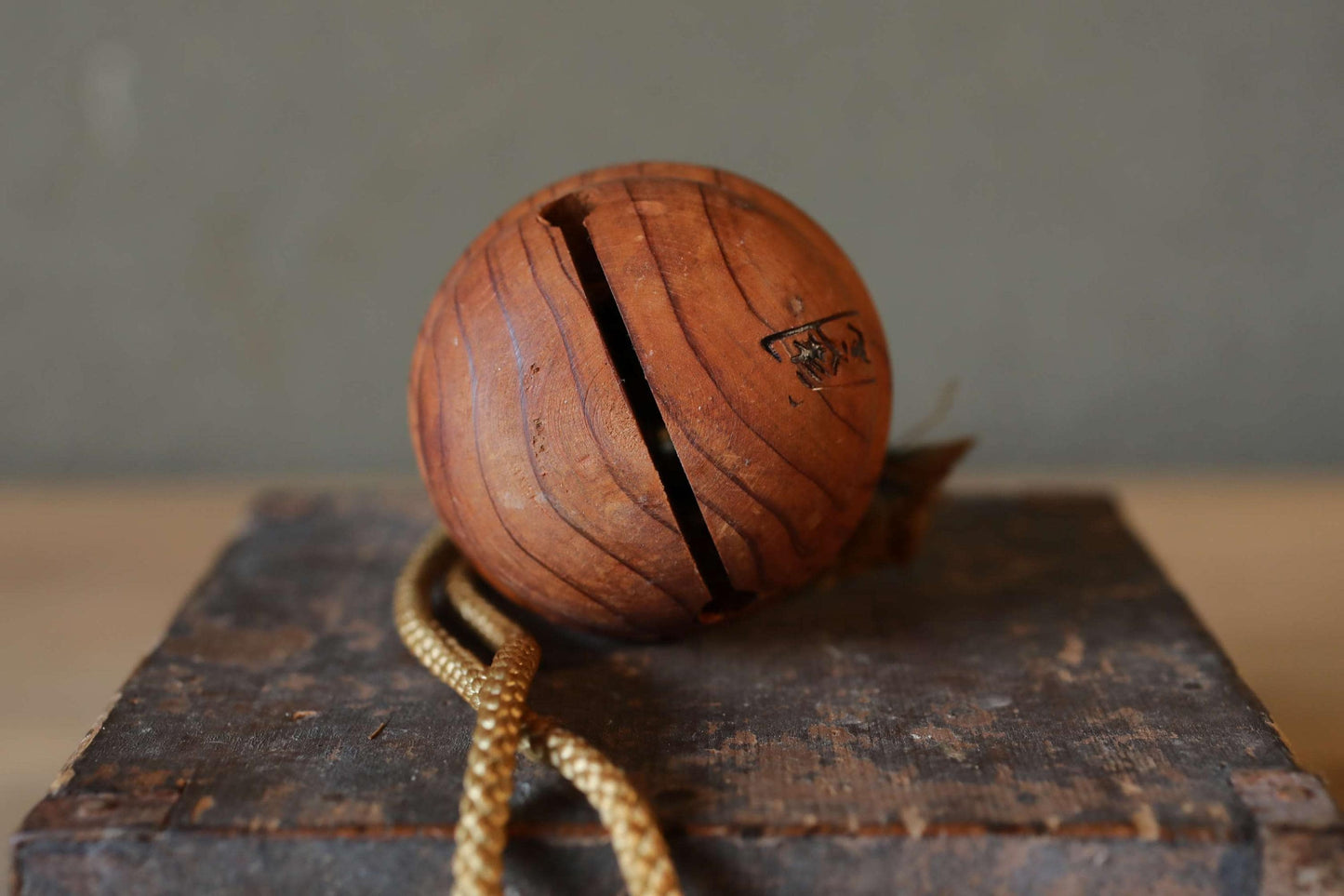 A wooden ball with a carved design sits on a wooden surface, accompanied by a rope.