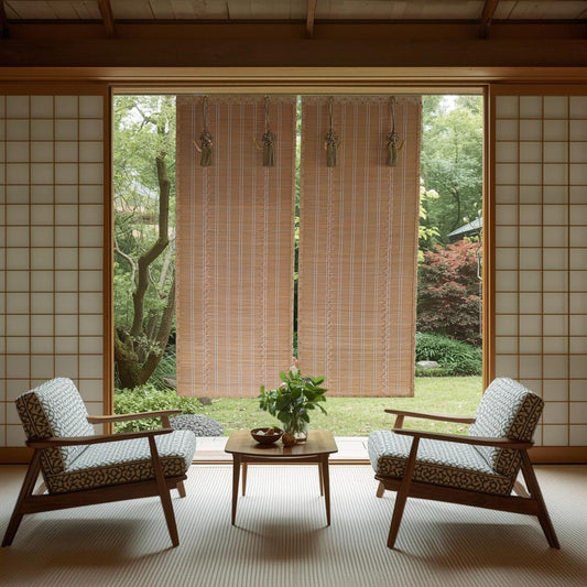 a serene and minimalist living space with a view of a lush garden through a large window. The room is furnished with two patterned armchairs and a wooden coffee table, creating a cozy seating area. The room is adorned with wooden blinds that allow natural light to filter in, and a small potted plant adds a touch of greenery to the space. The overall design and layout of the room create a harmonious and tranquil atmosphere.
