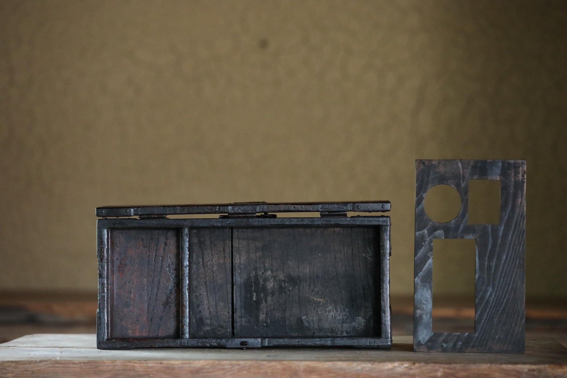 a wooden box with a metal frame, placed on a wooden surface against a textured wall background.