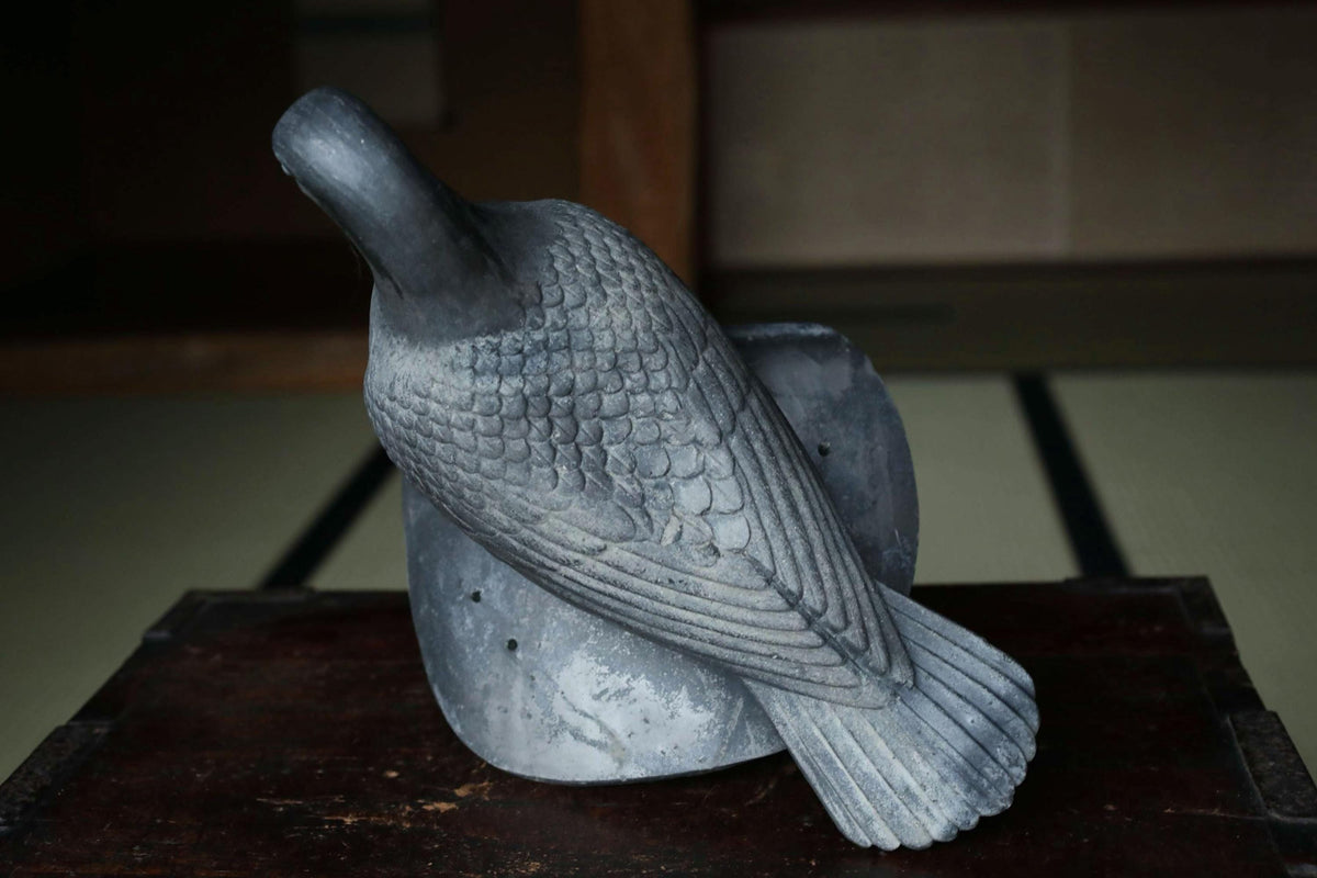 A gray stone sculpture of a bird, possibly a crane, is displayed on a wooden surface.