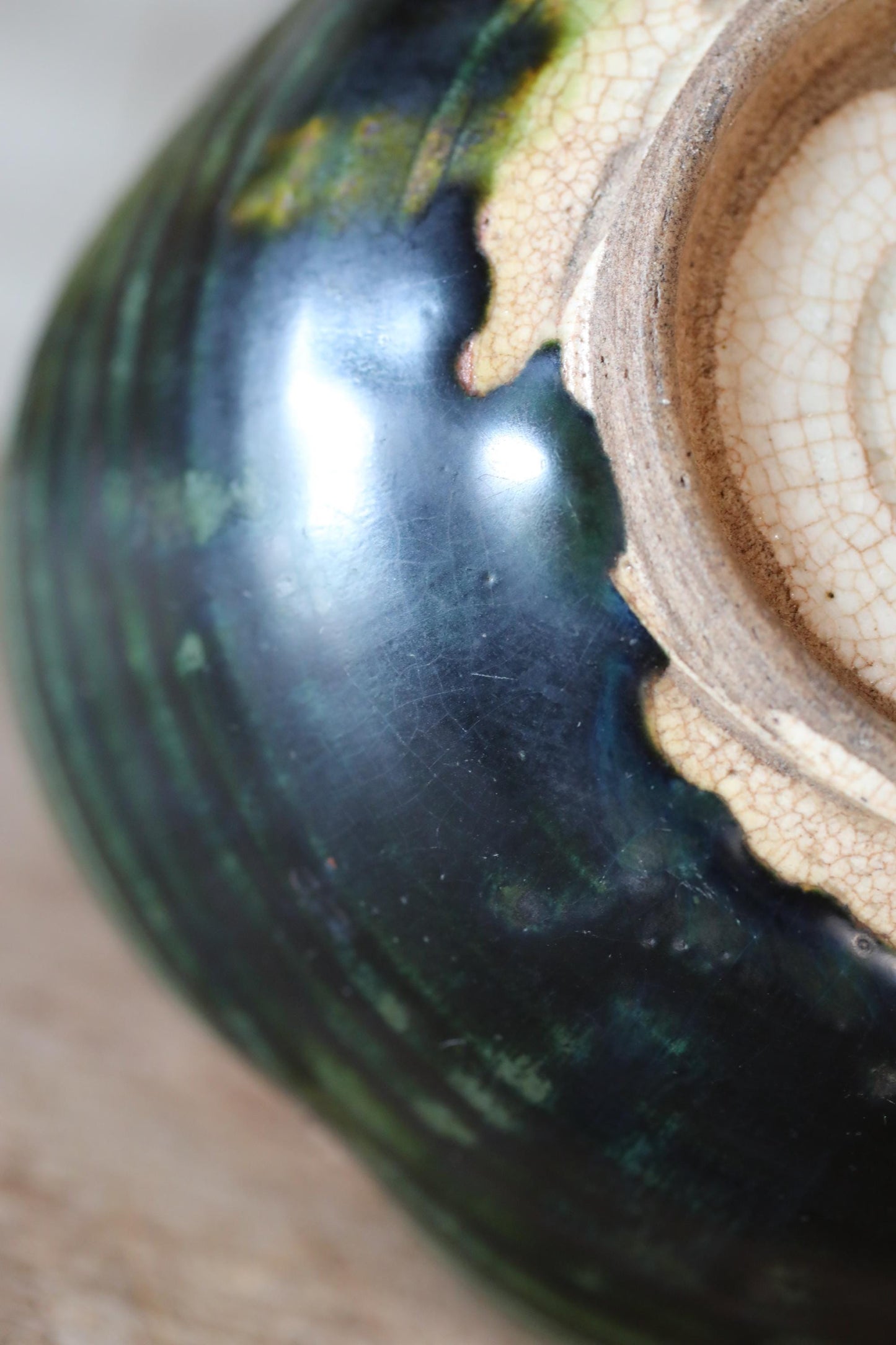 A close-up view of a ceramic vase with a dark green and blue color scheme, featuring a textured surface and a white rim.