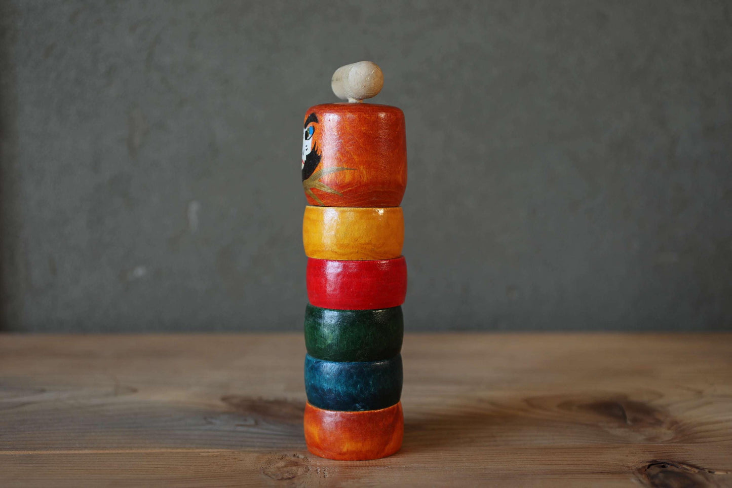 A colorful wooden toy with a bird design sits on a wooden surface against a gray background.