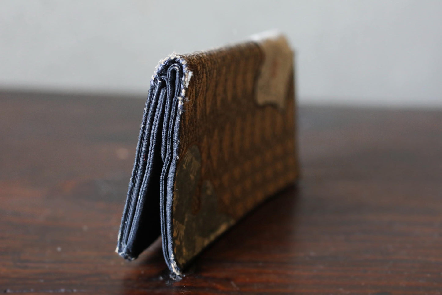 A brown wallet with a patterned design sits on a wooden surface.