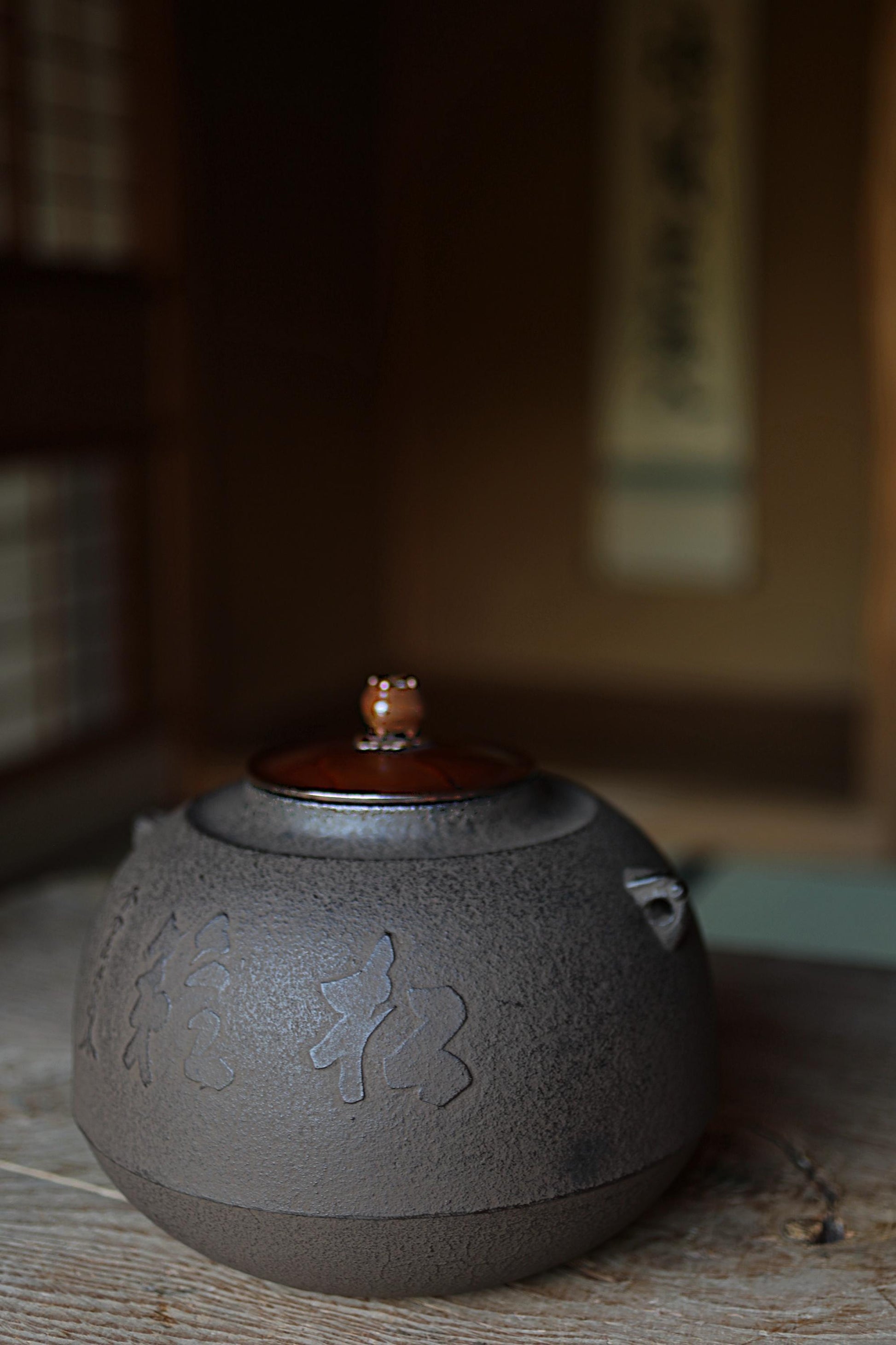 A dark gray ceramic teapot with a lid and a small handle, sitting on a wooden surface.