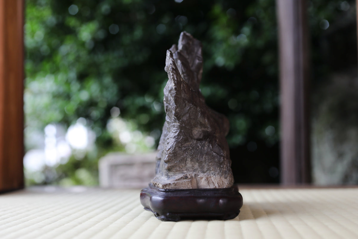 A close-up image of a stone sculpture on a wooden base, placed on a wooden surface.