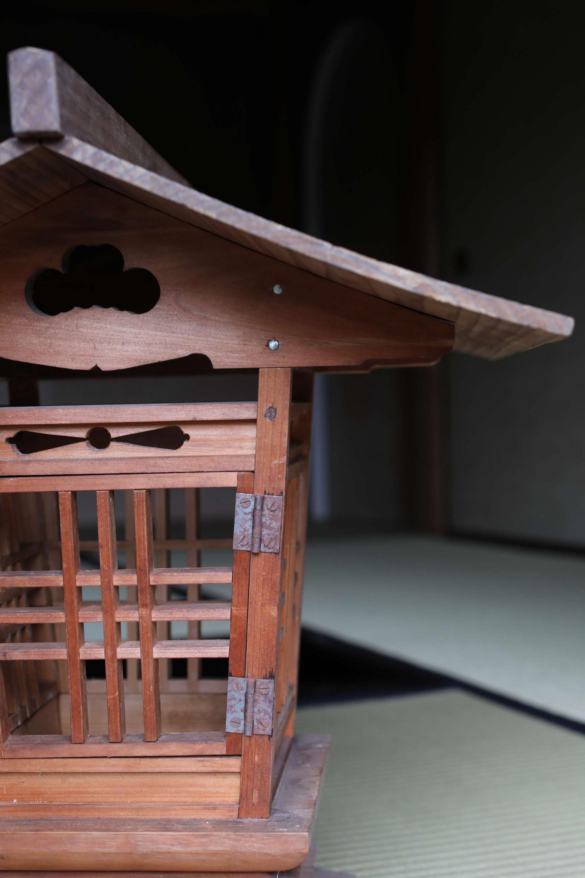 A wooden Japanese-style lantern or pagoda-like structure with intricate carvings and a sloping roof, situated in a dimly lit room.