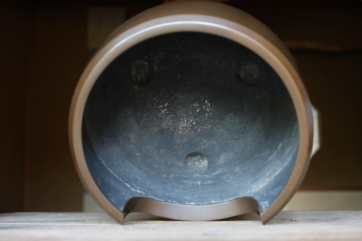 a close-up view of a metal pot with a dark interior, sitting on a wooden surface.