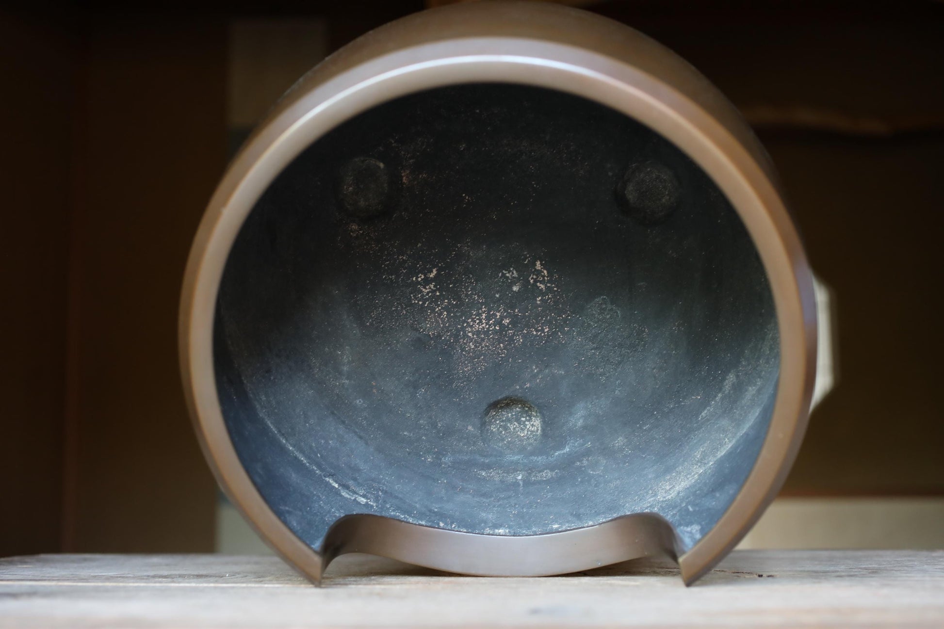 a close-up view of a metal pot with a dark interior, sitting on a wooden surface.