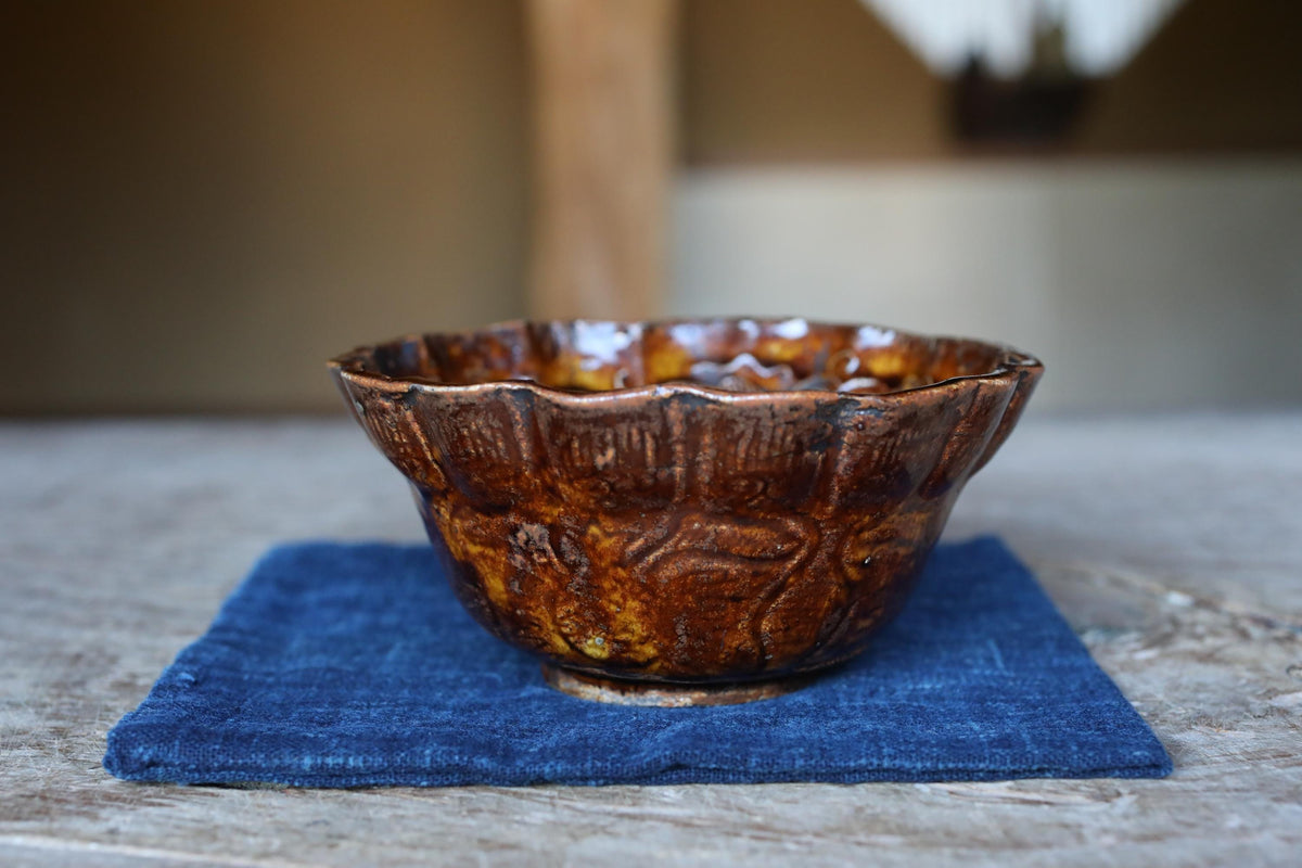 A brown ceramic bowl with a scalloped edge sits on a blue cloth on a wooden surface.
