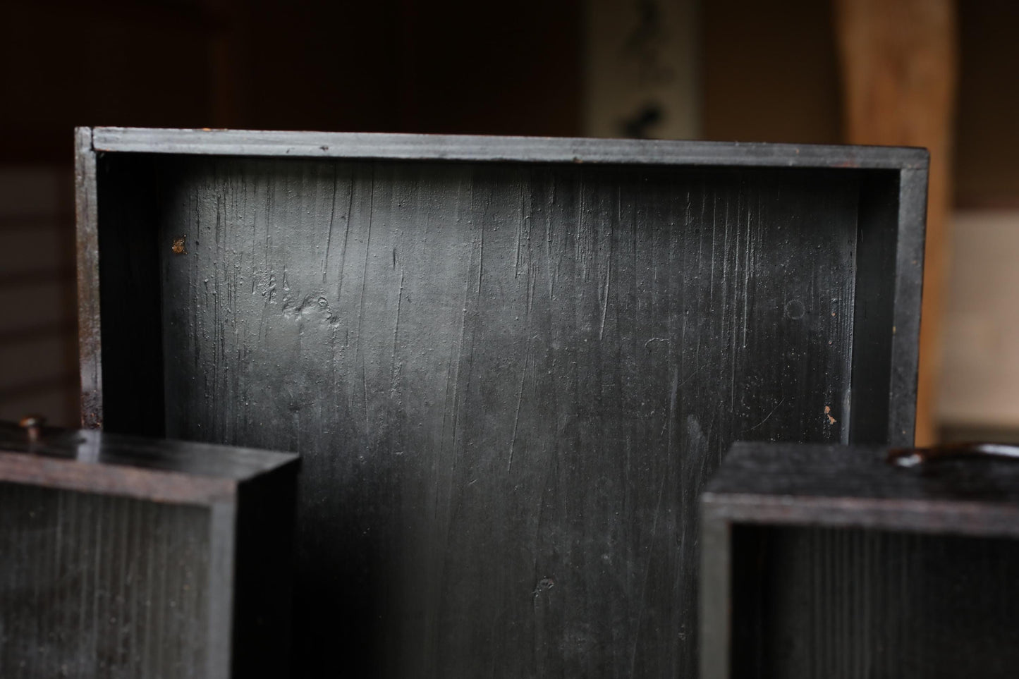 a close-up view of a dark wooden box or container, with a textured surface and a slightly rusted appearance.