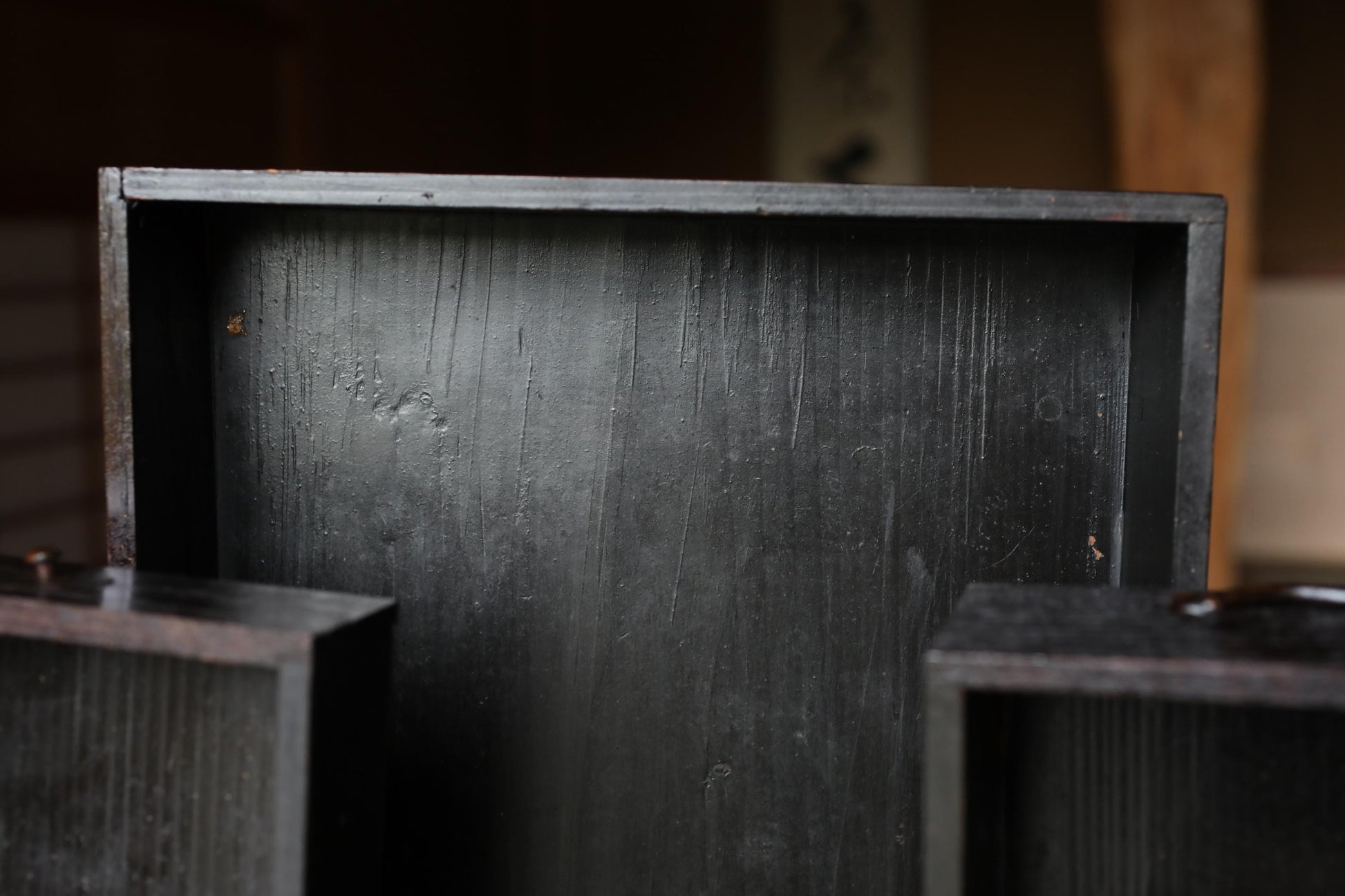 a close-up view of a dark wooden box or container, with a textured surface and a slightly rusted appearance.