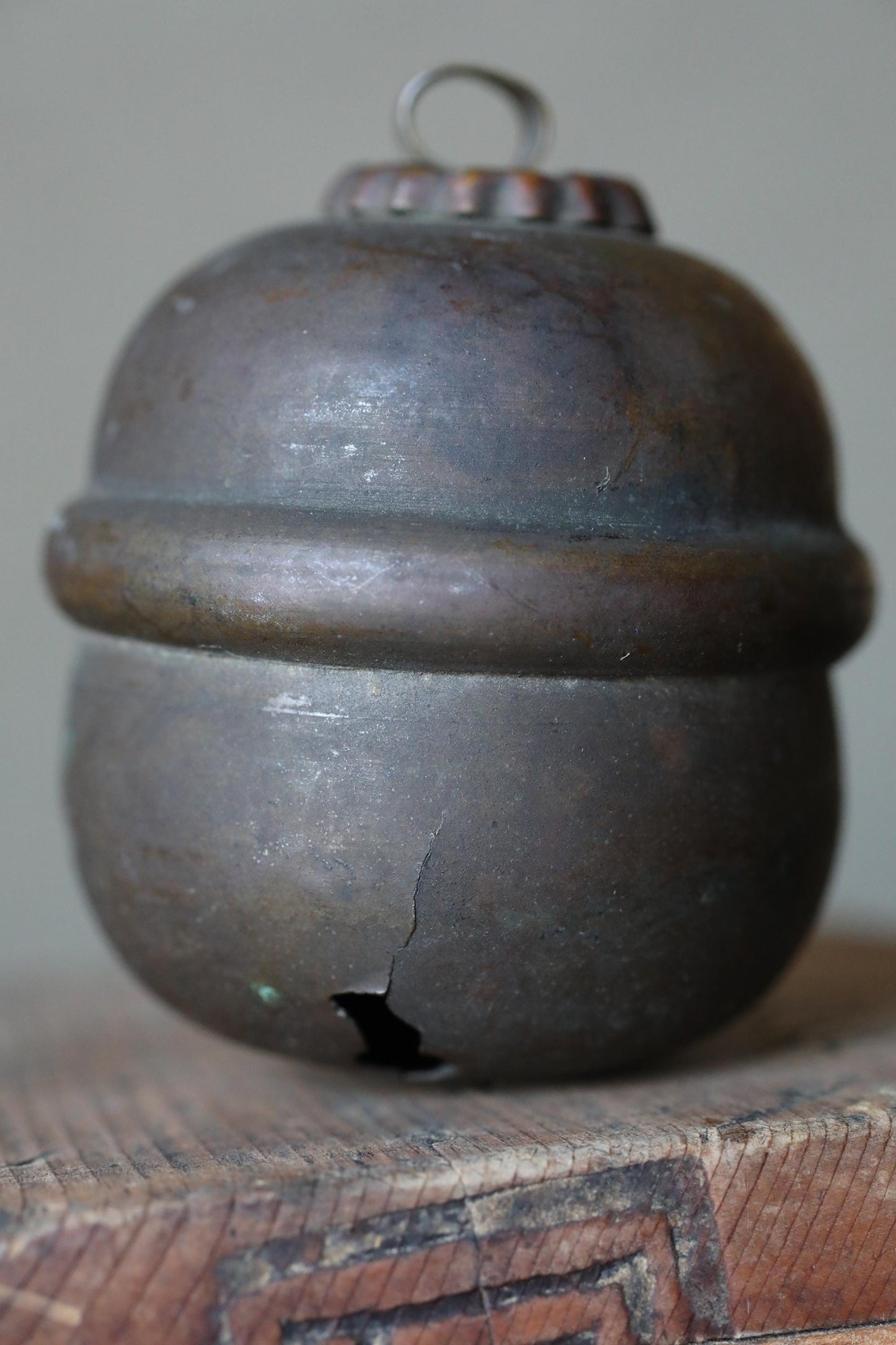 A close-up image of a rusted metal object, possibly a bell or container, sitting on a wooden surface.