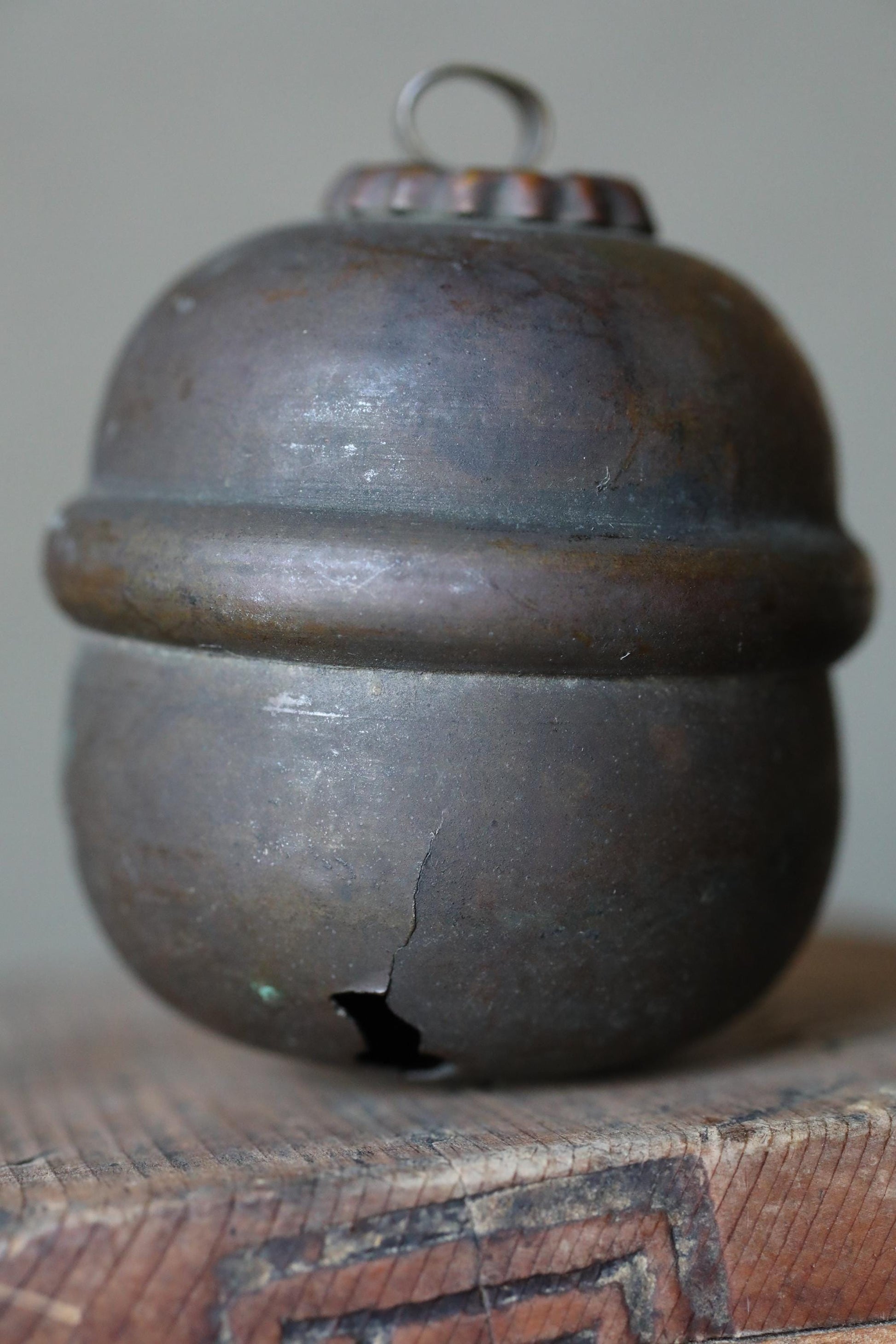 A close-up image of a rusted metal object, possibly a bell or container, sitting on a wooden surface.