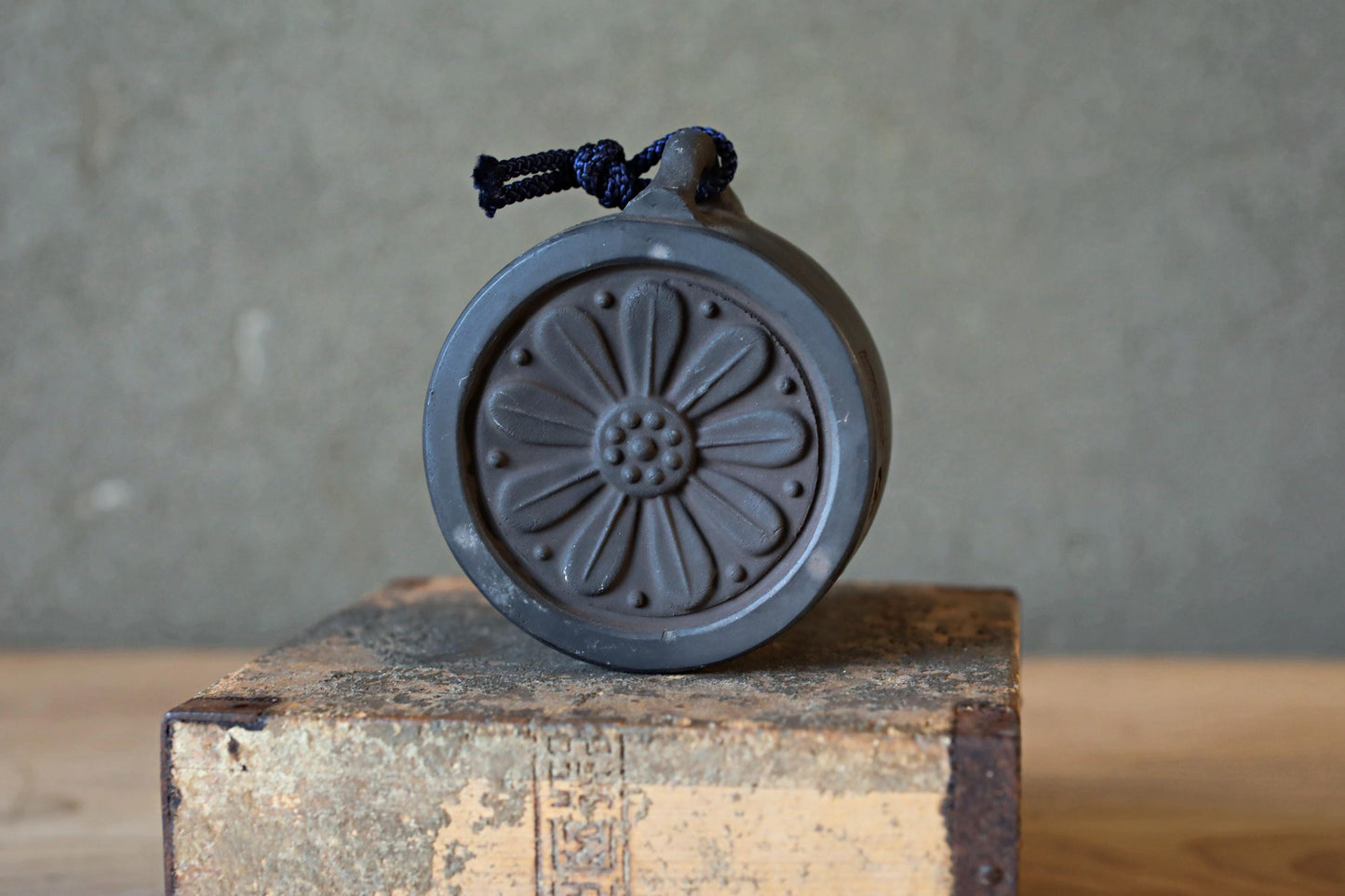 A black metal object with a flower-like design on it, sitting on a wooden surface against a gray background.