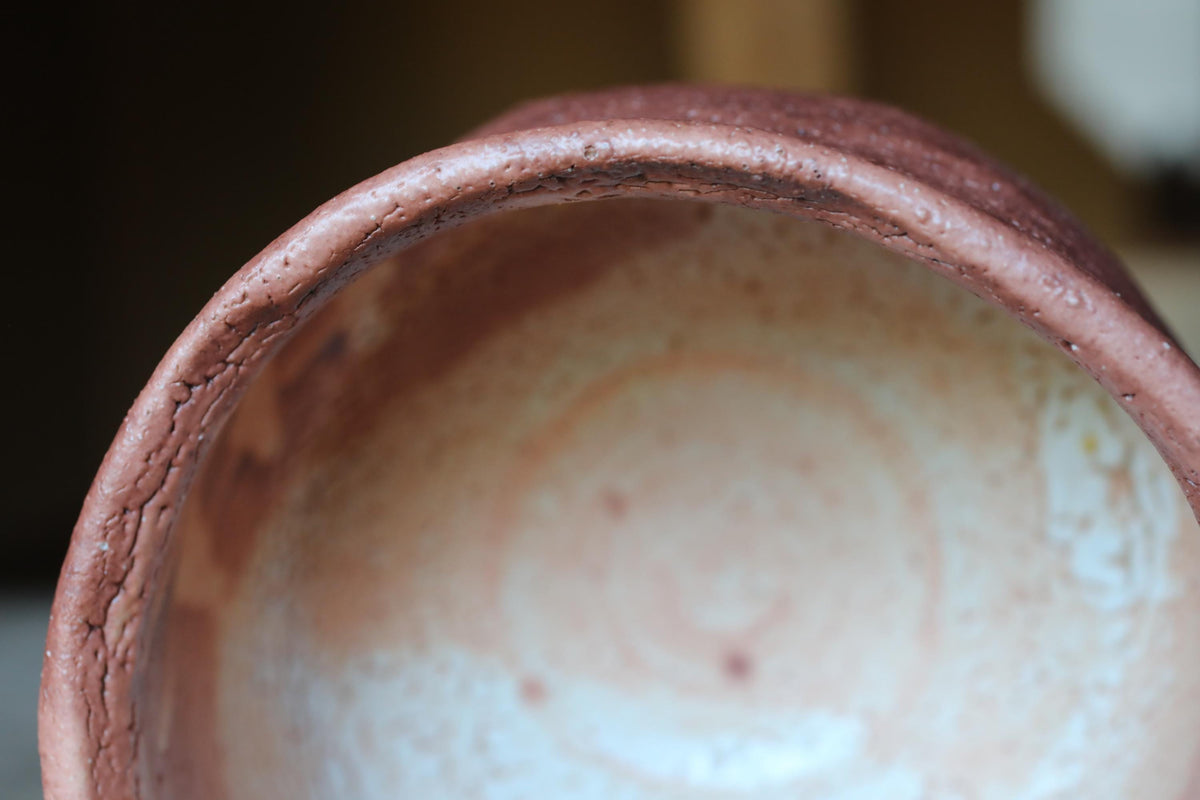 A close-up view of a ceramic bowl with a reddish-brown hue and a white interior, featuring a circular pattern on the surface.