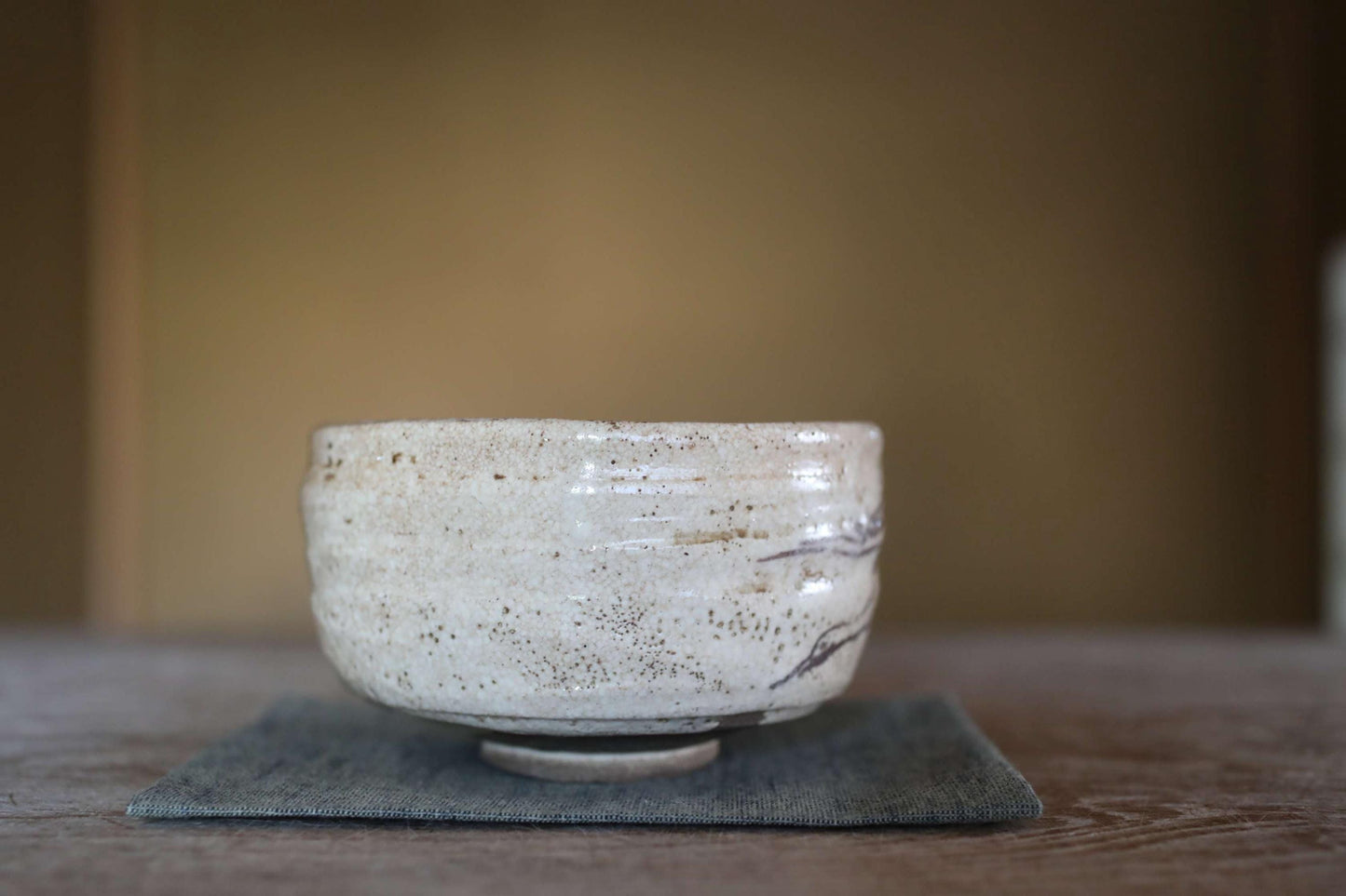 A white ceramic bowl with a textured surface sits on a gray cloth on a wooden table.