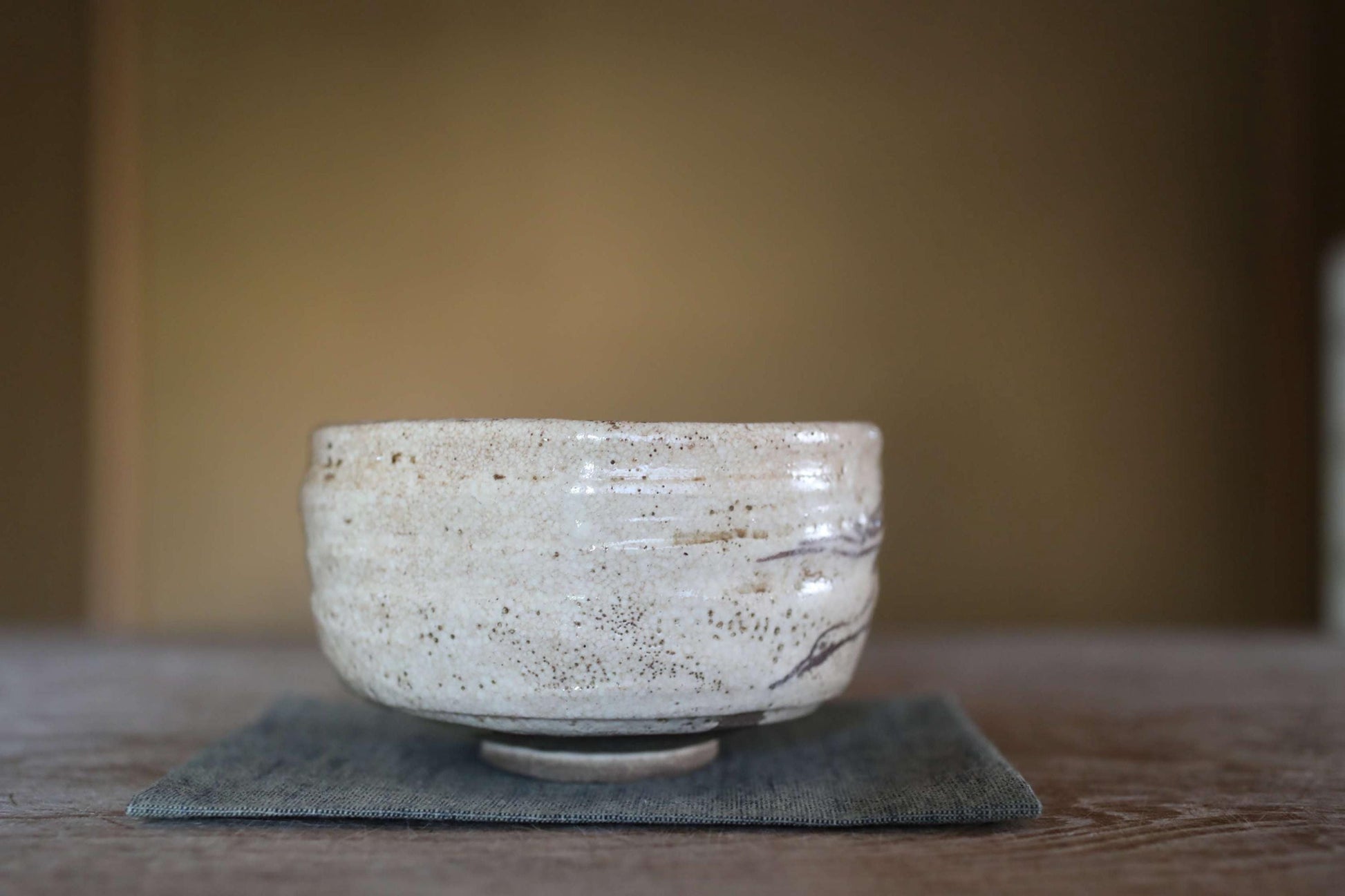 A white ceramic bowl with a textured surface sits on a gray cloth on a wooden table.