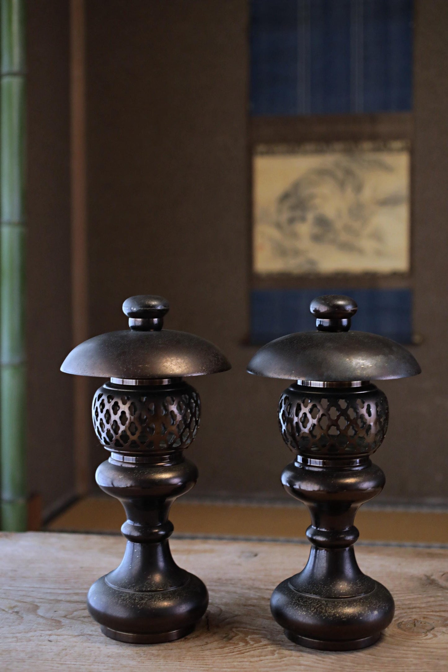 two ornate, black metal lanterns with intricate designs, placed on a wooden surface.