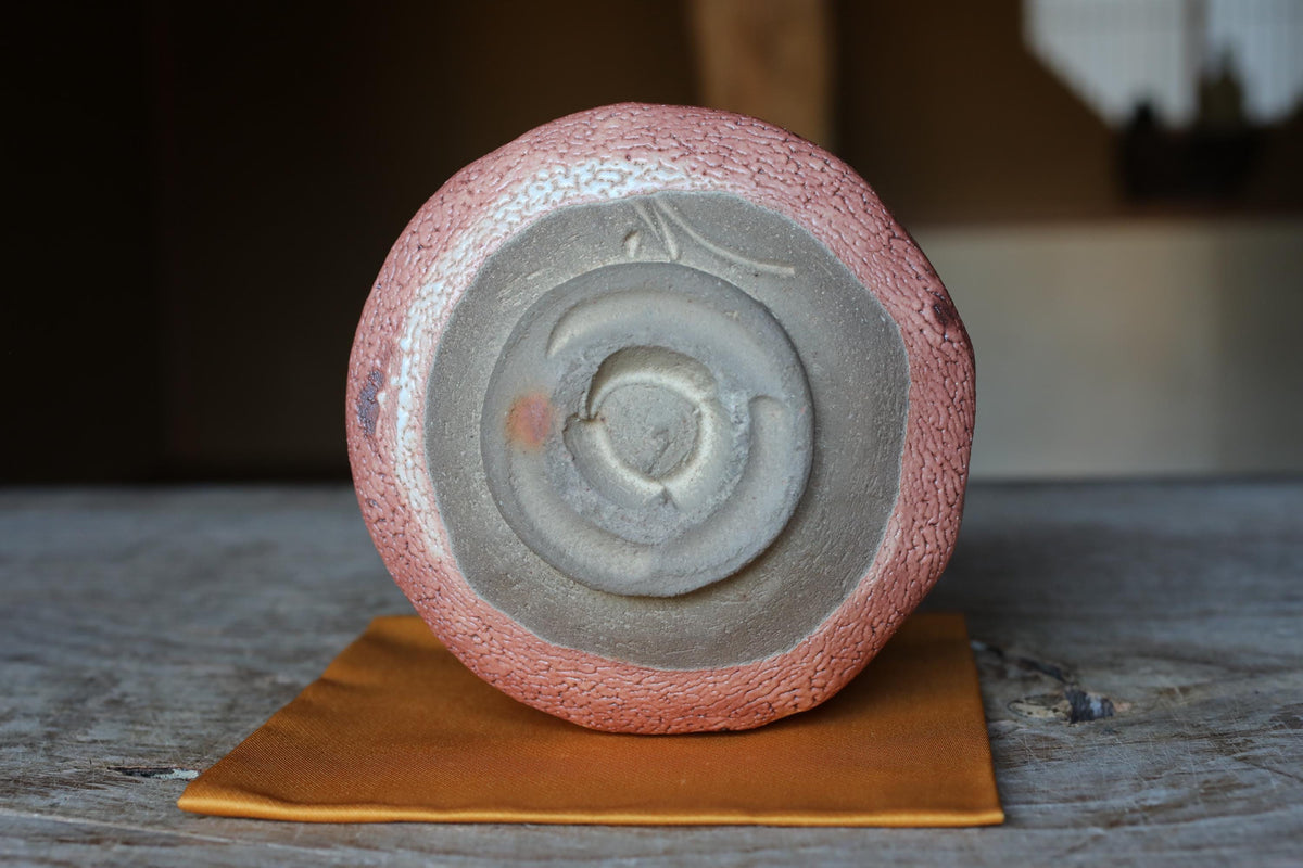 A ceramic object with a textured surface and a circular design in the center, placed on a wooden surface with a yellow cloth underneath.