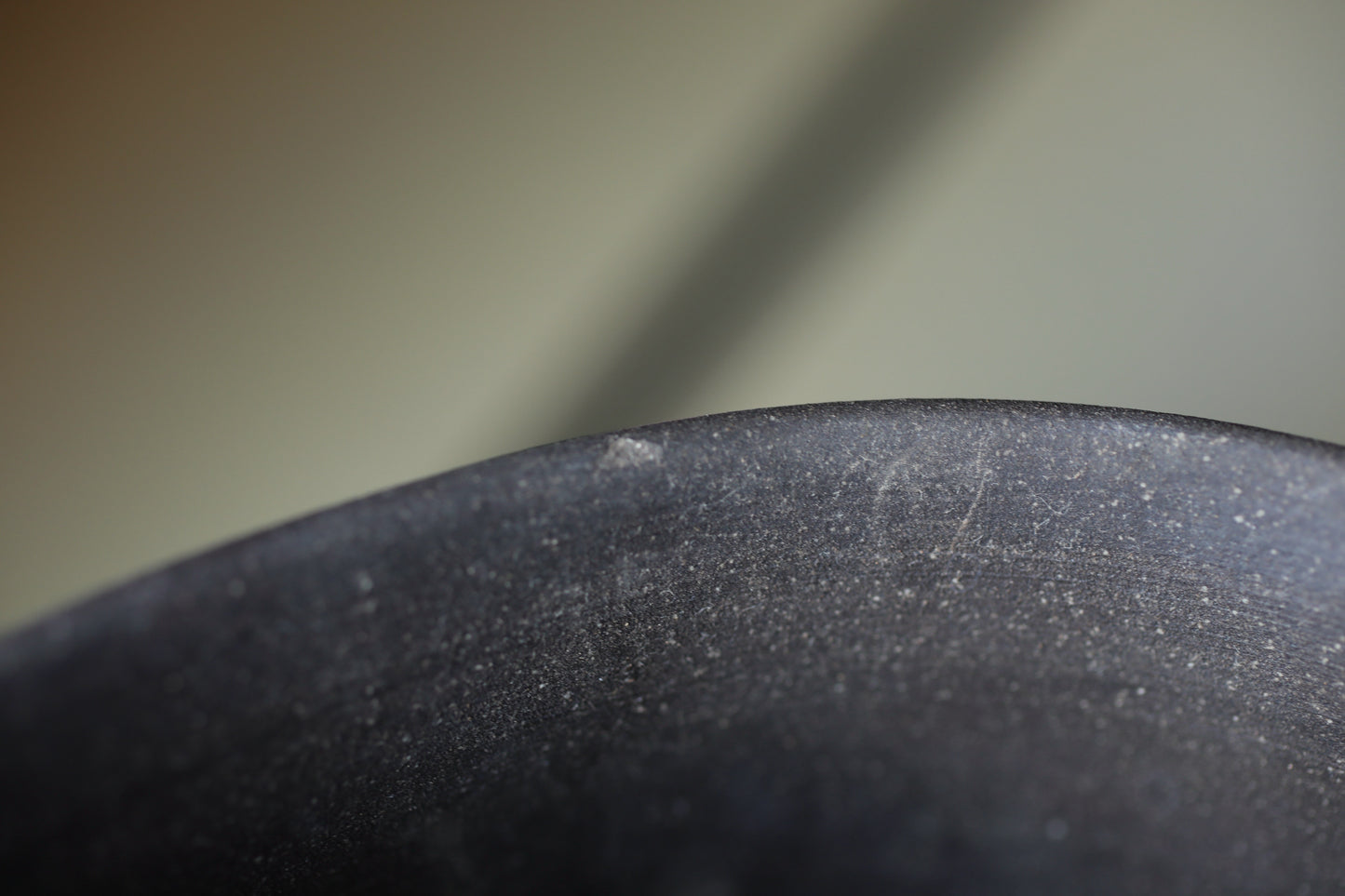 a close-up view of a black, textured surface, possibly a piece of pottery or a metal object. The surface appears to be dirty or stained, with visible scratches and marks. The background is blurred, drawing focus to the subject in the foreground.
