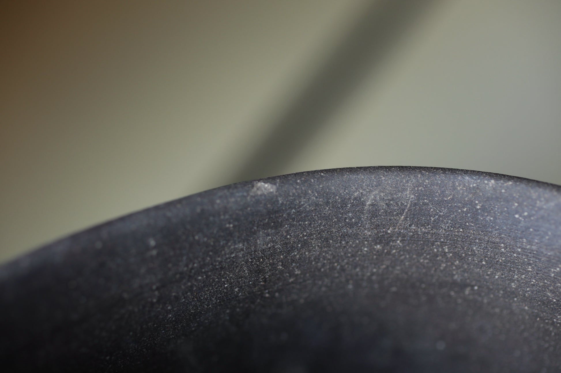 a close-up view of a black, textured surface, possibly a piece of pottery or a metal object. The surface appears to be dirty or stained, with visible scratches and marks. The background is blurred, drawing focus to the subject in the foreground.