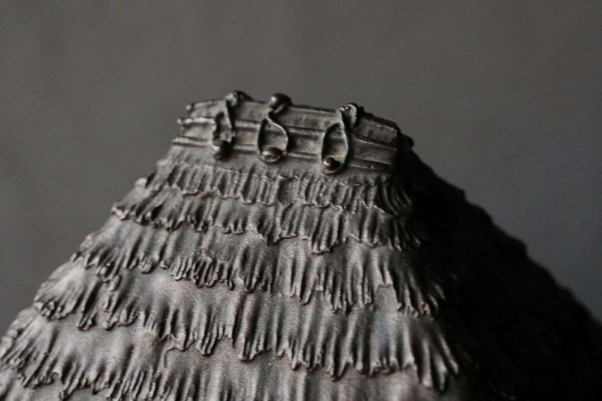 A close-up view of a textured, dark-colored surface with a repeating pattern of lines and shapes, resembling a piece of art or a decorative element.