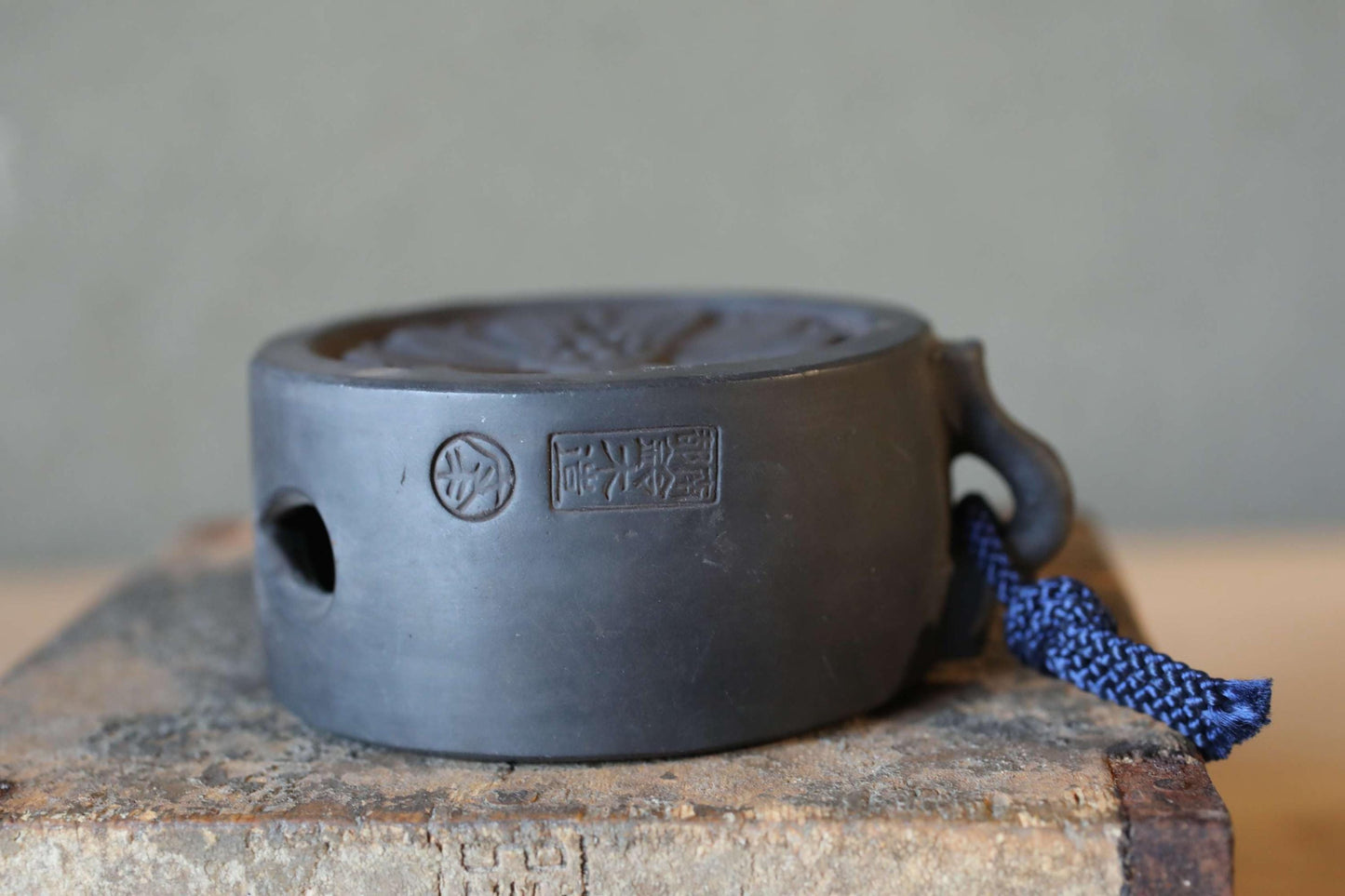 A black ceramic object with a blue string attached to it, sitting on a wooden surface.