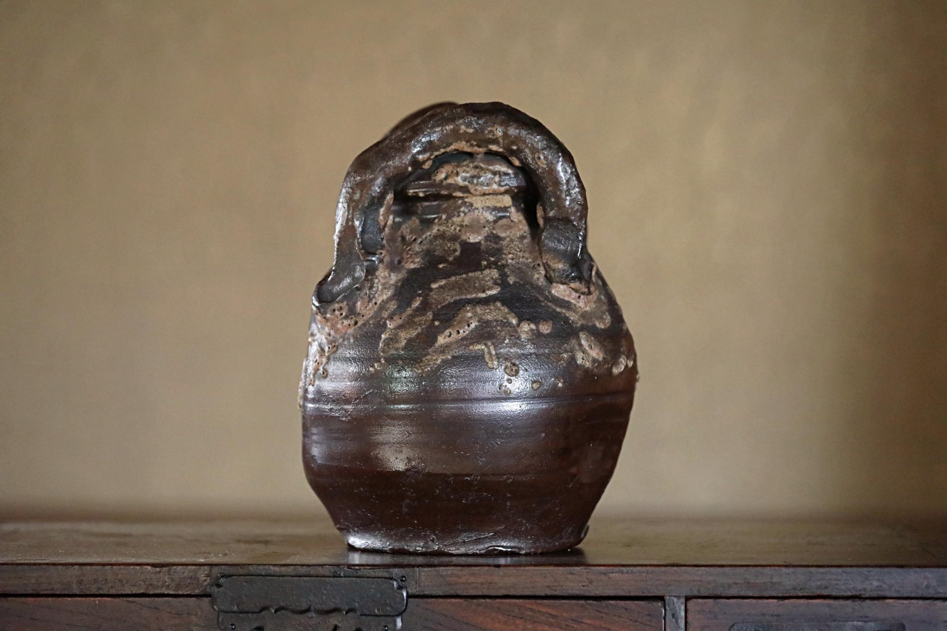 A dark brown ceramic vase with a unique, twisted shape sits on a wooden surface.